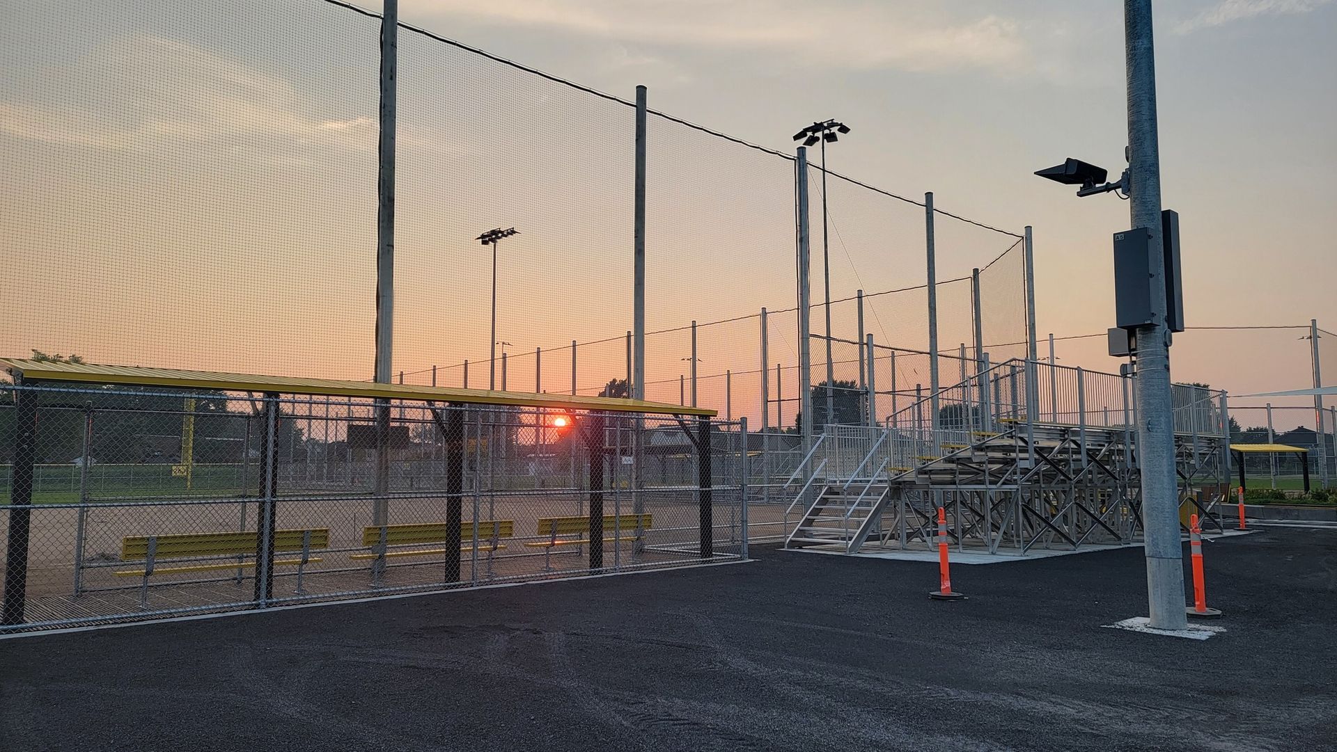 Chain-link fence surrounding an industrial area with power lines and light poles at sunset.
