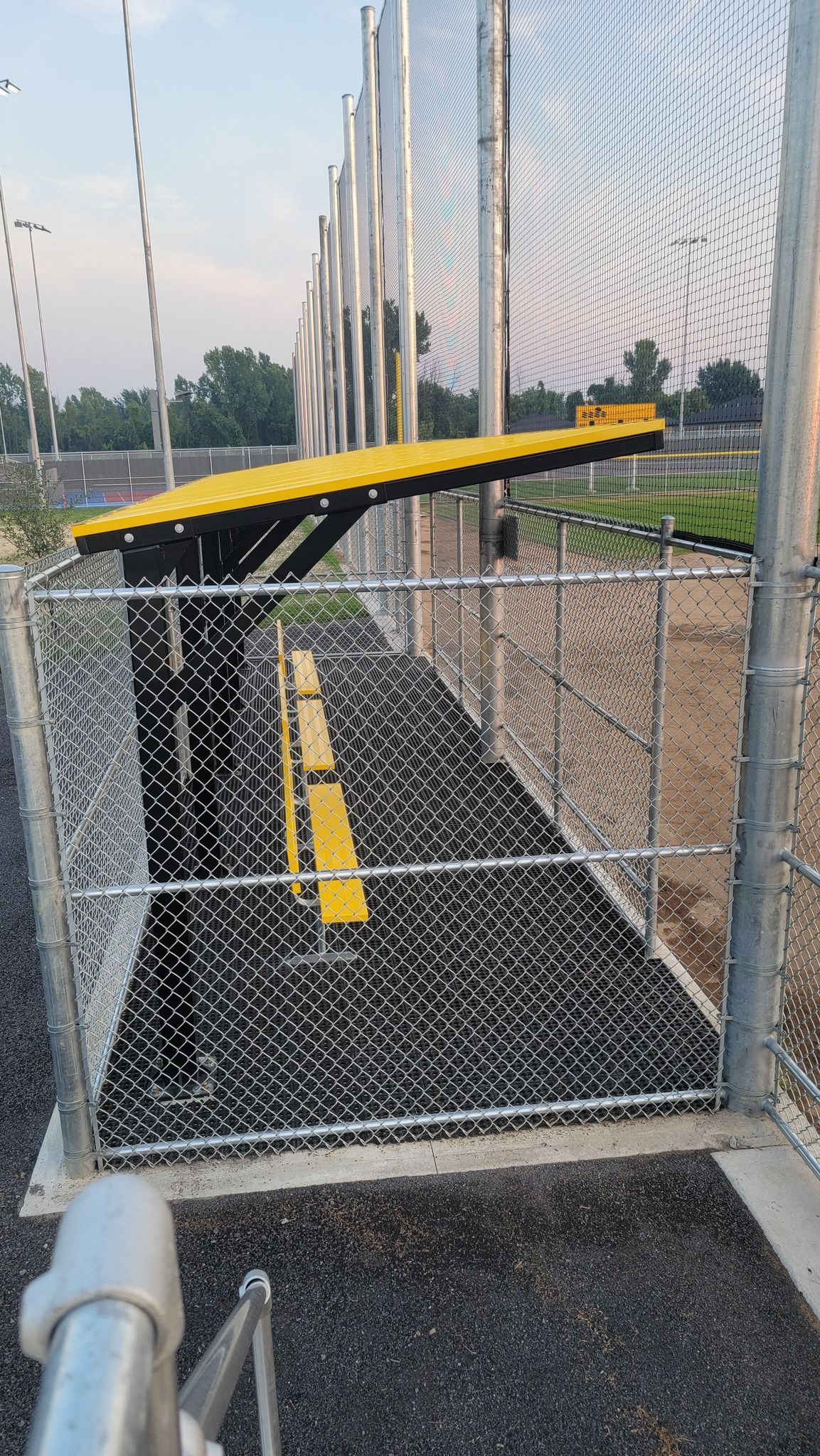 Yellow batting cages within a chain-link fence, with a ground-level view of the walkway and supports.