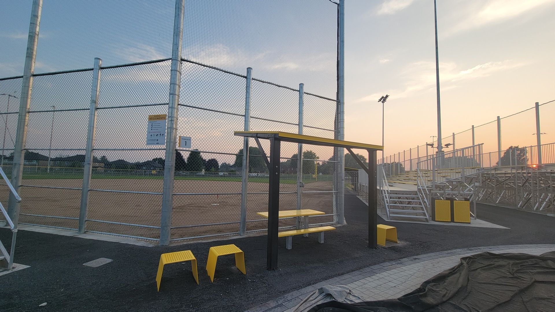 Baseball field with protective netting and yellow seating. Evening sky.