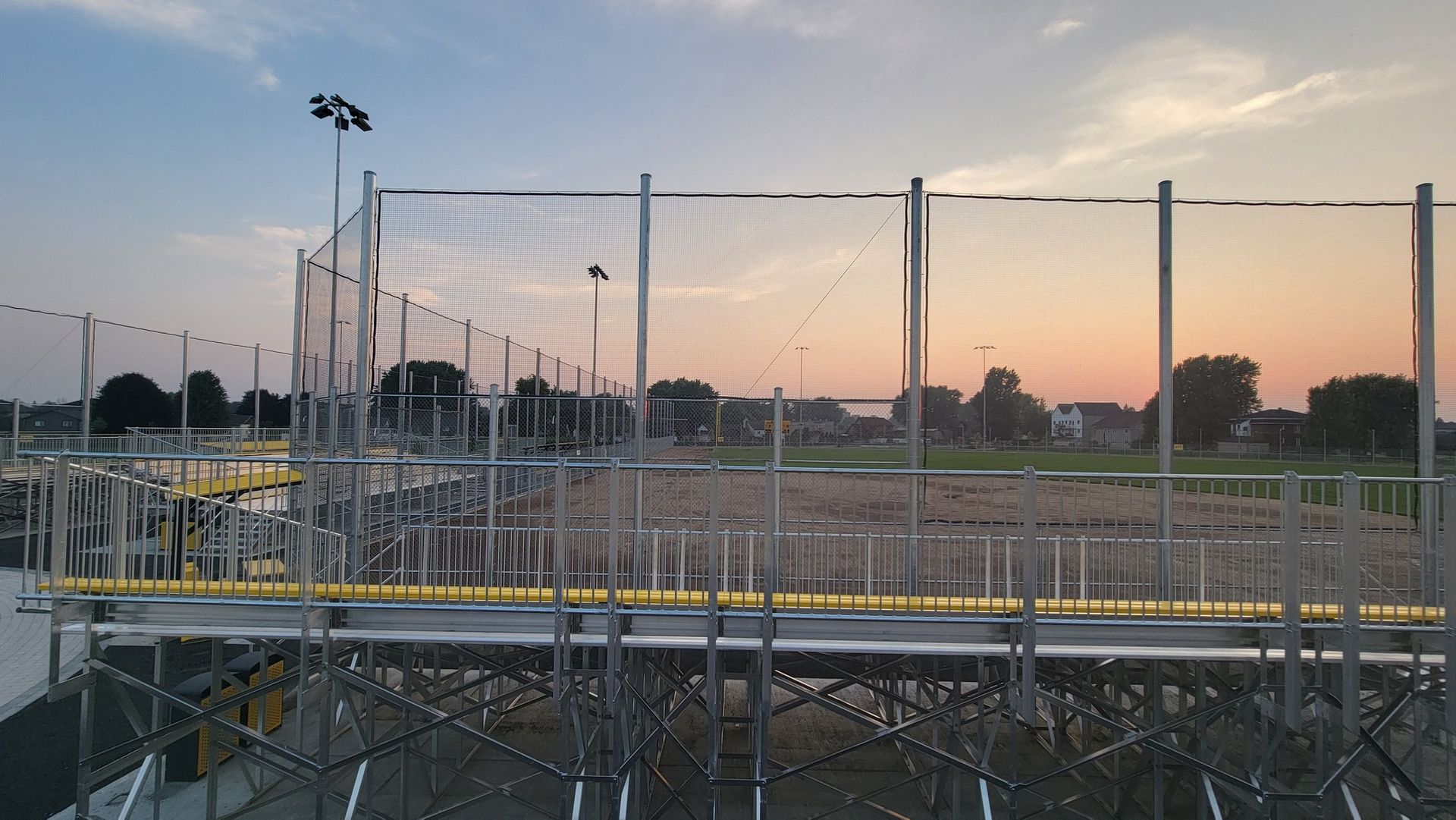 Bleachers and protective netting at a baseball field during sunset.