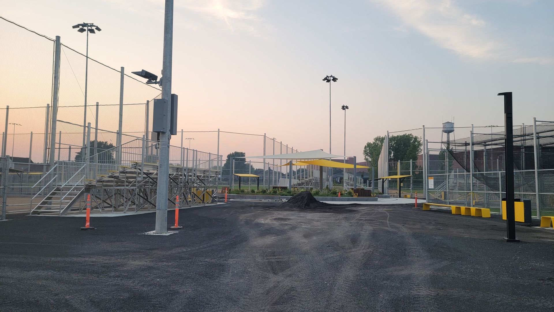 Open-air sports facility with fencing, lights, and black asphalt. Gray sky in the background.