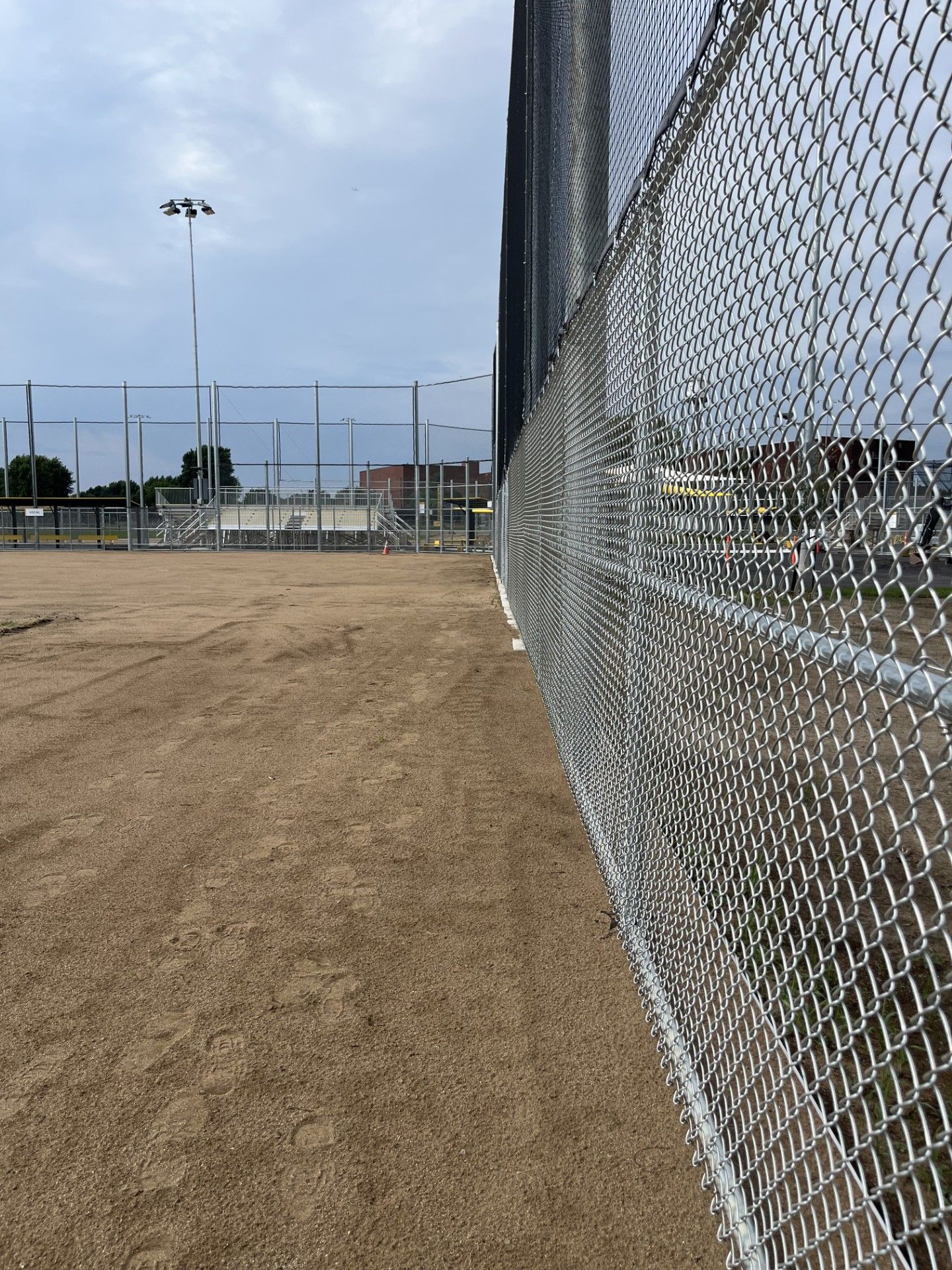 Chain-link fence borders a baseball field with a dirt surface. A light post is visible in the background.