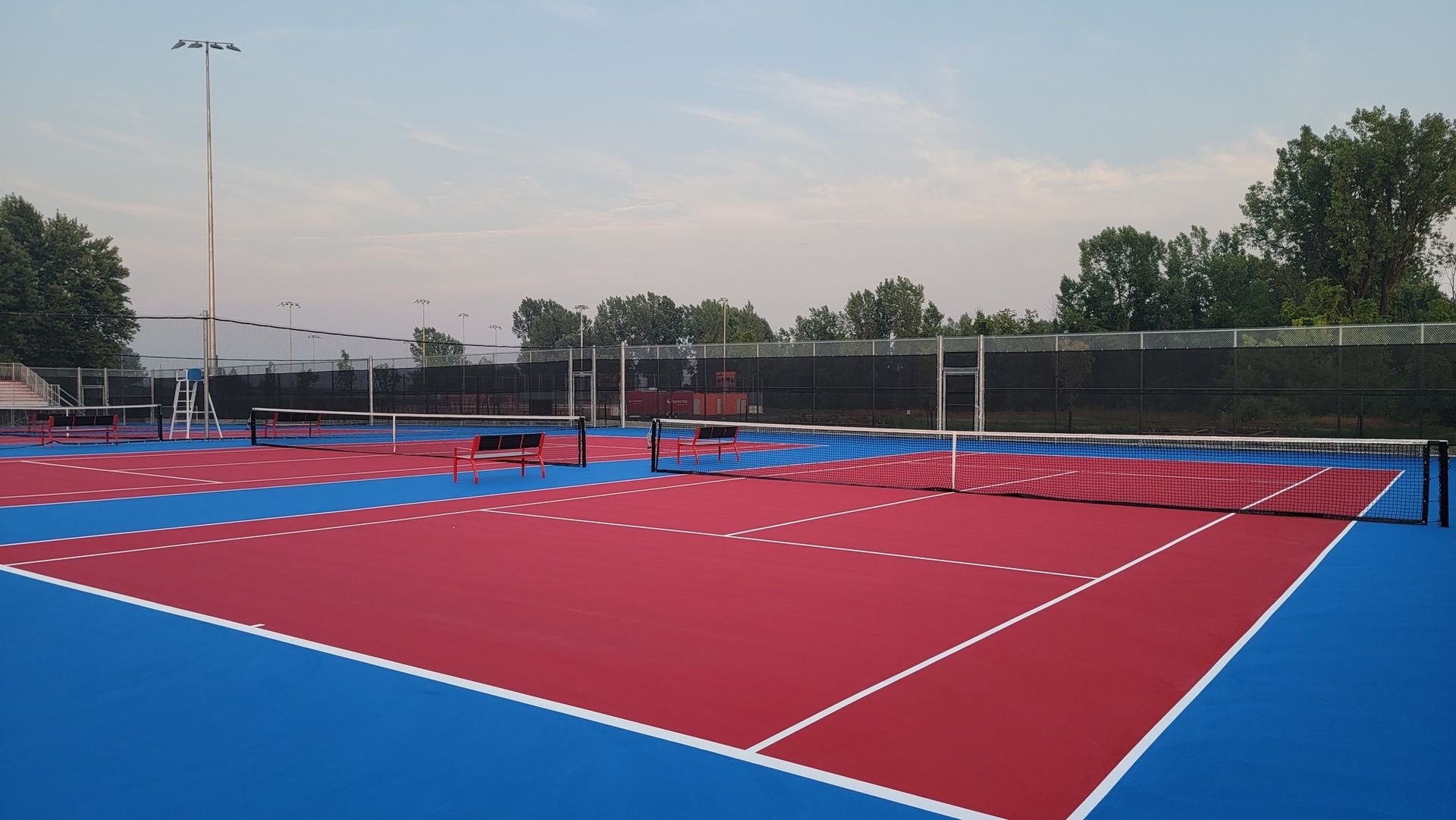 Red and blue outdoor sports court with volleyball nets under a partly cloudy sky.