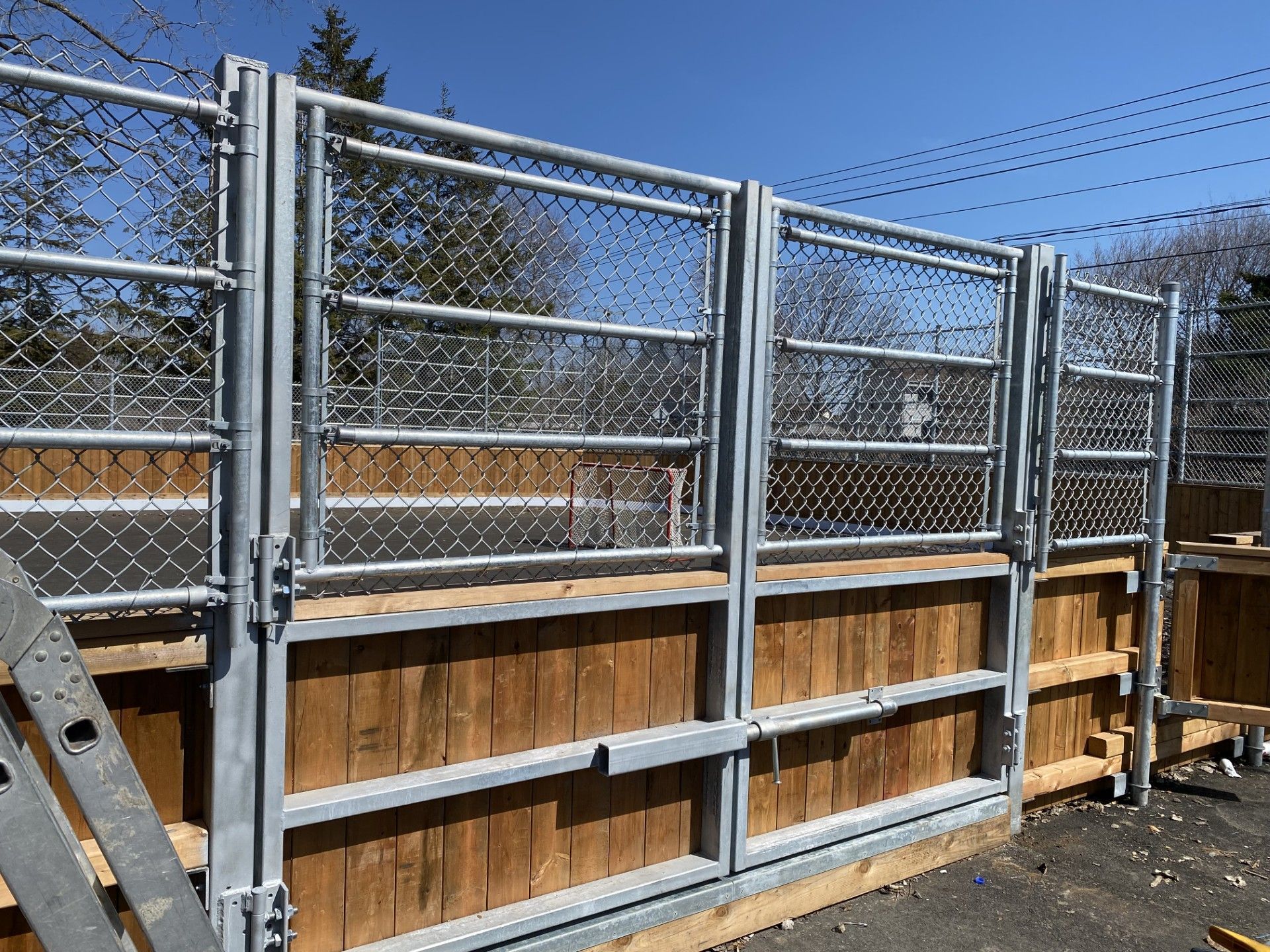Chain-link and metal gate fence atop wooden base. Outdoors, bright day.