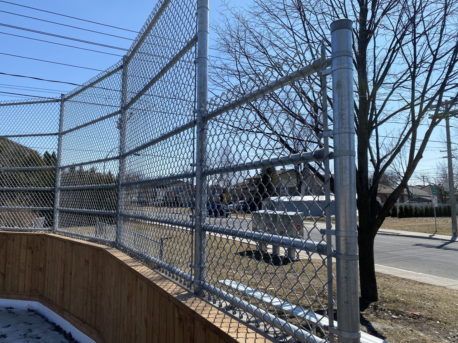 Chain-link fence on a wooden base next to a road, clear sky in background.