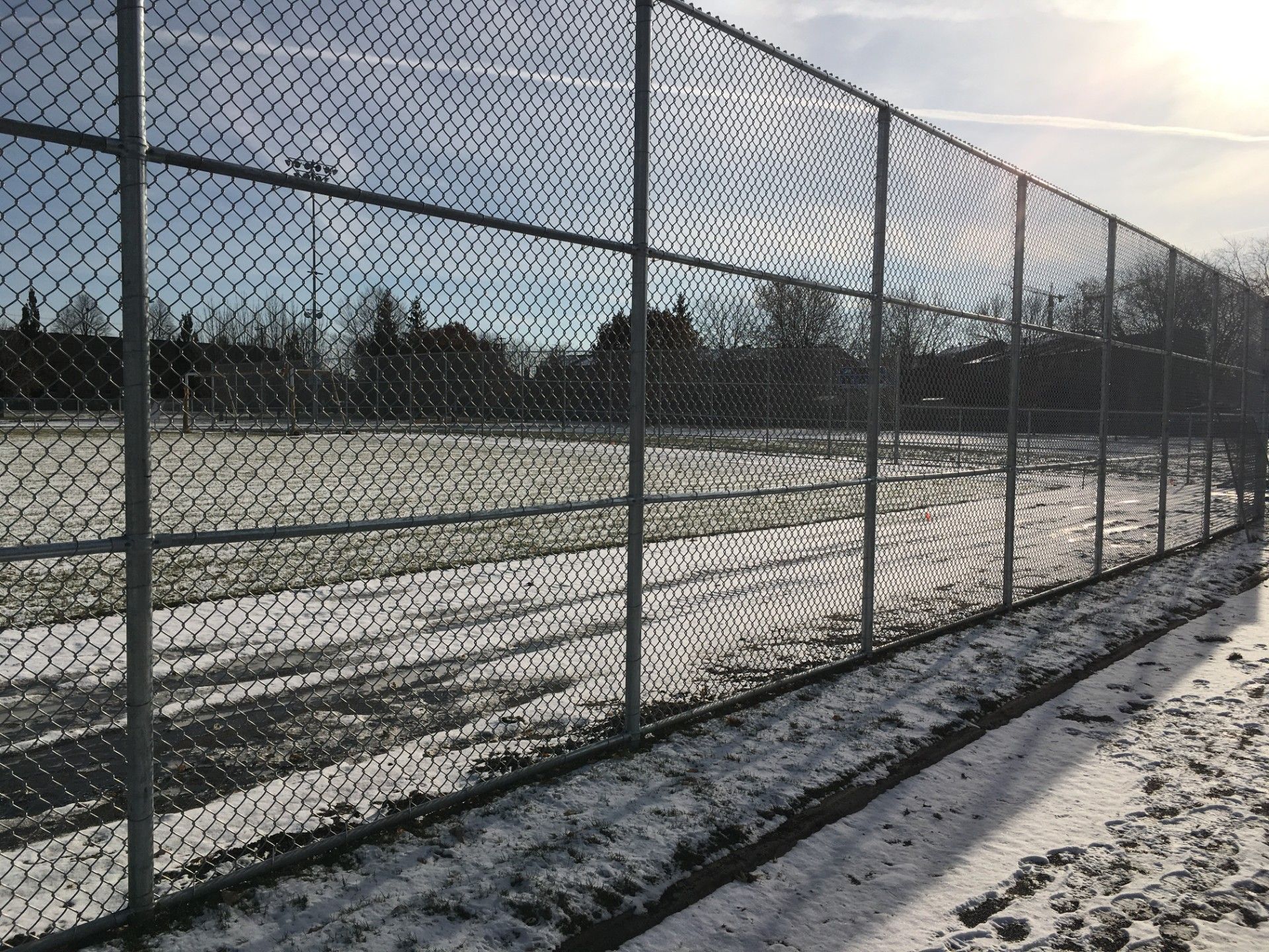 Chain-link fence borders a snow-covered field under a bright, sunny sky.