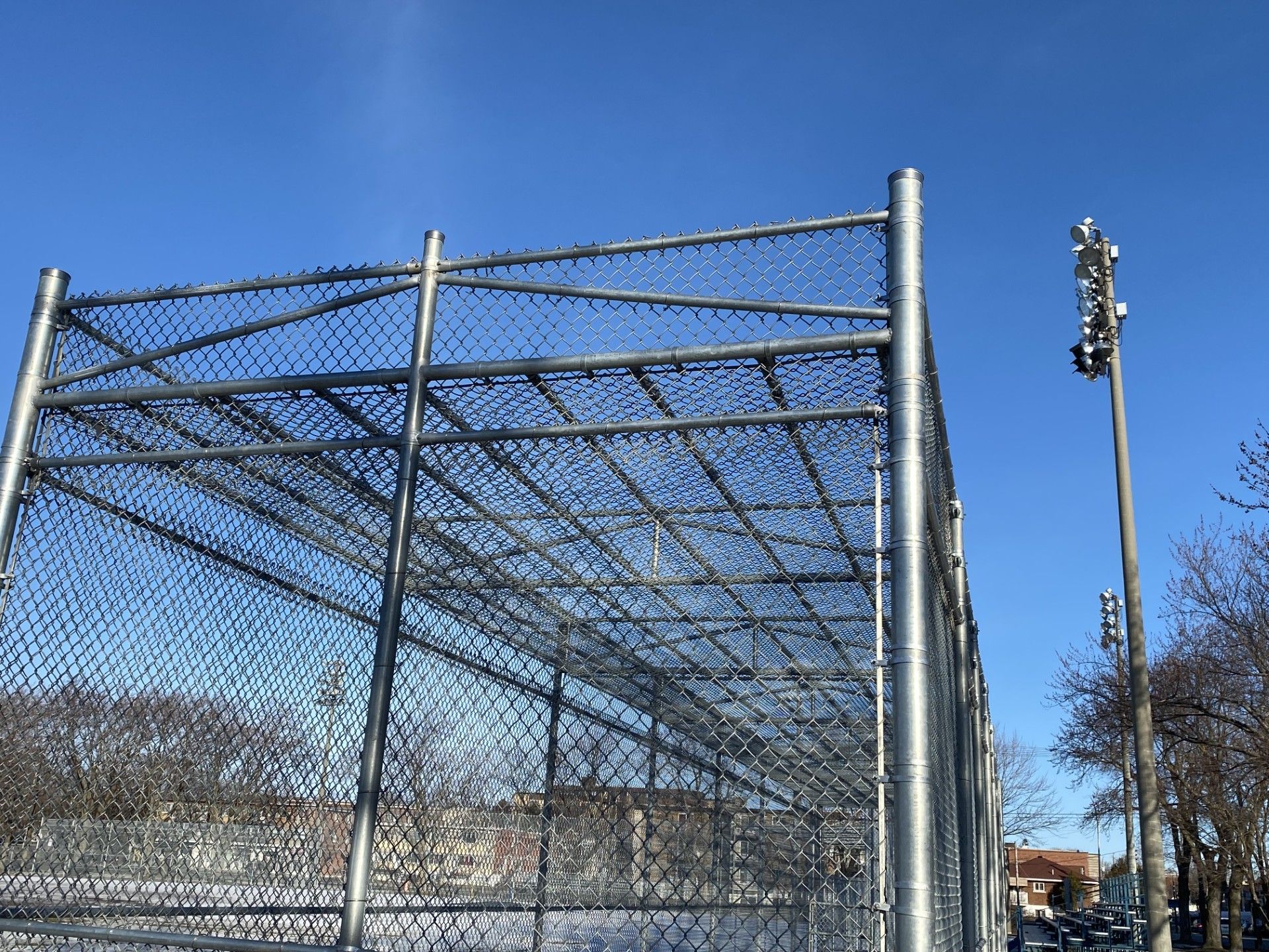 A chain-link fence encloses a structure against a clear blue sky. A light pole stands nearby.