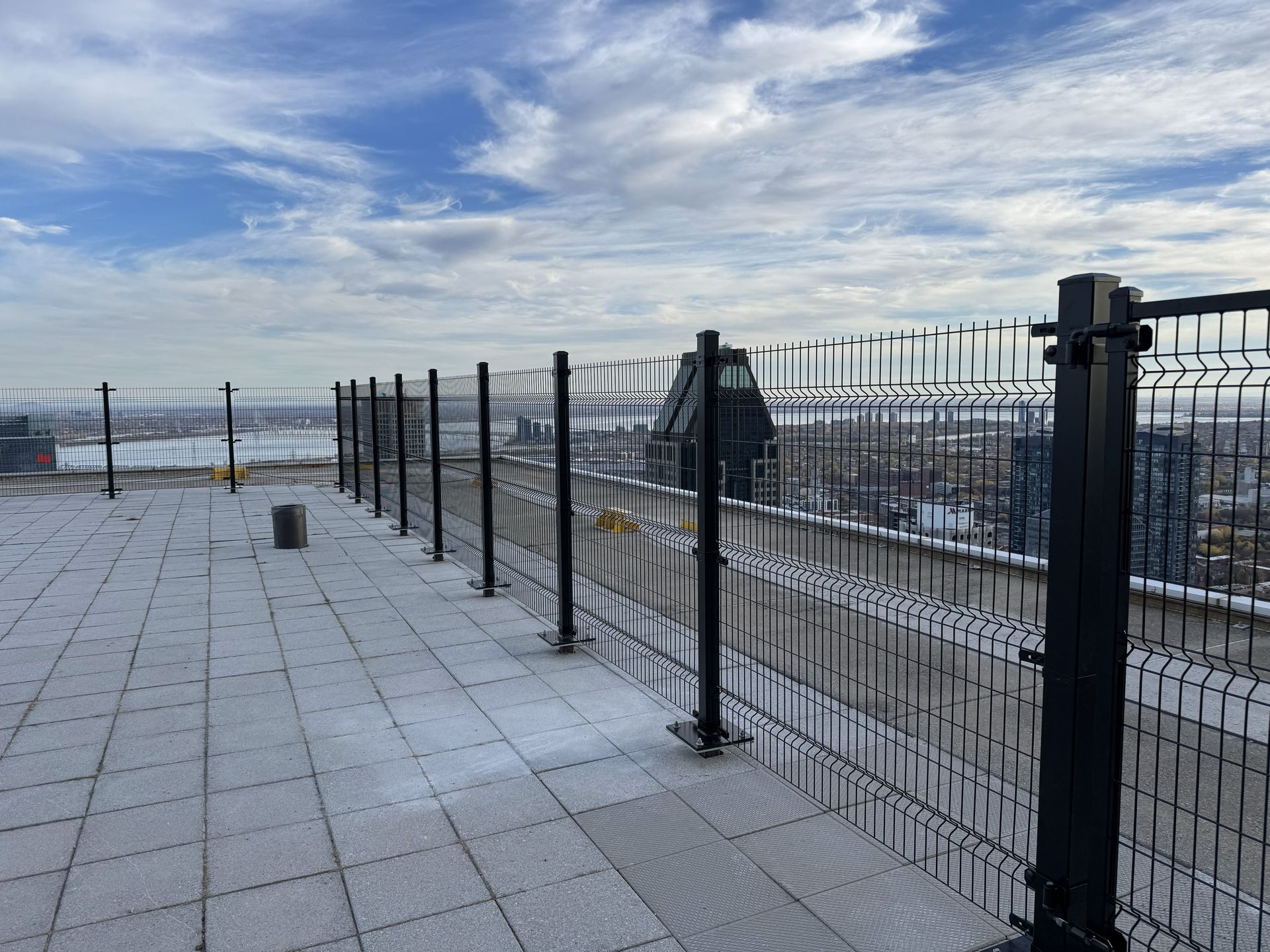Rooftop view with metal fence, cloudy sky, city buildings in the distance.