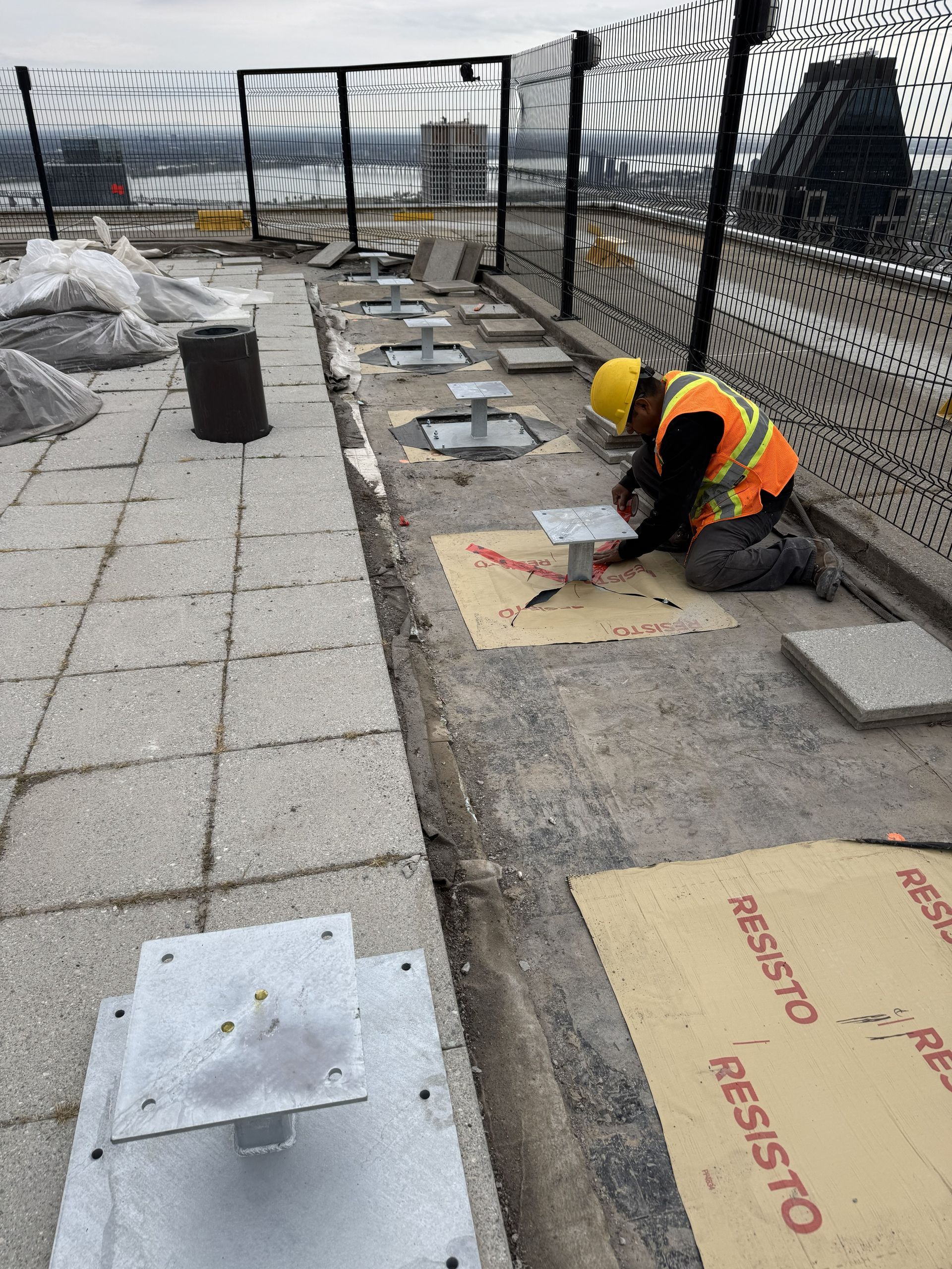 Construction worker in yellow hard hat, kneeling on rooftop installing equipment.