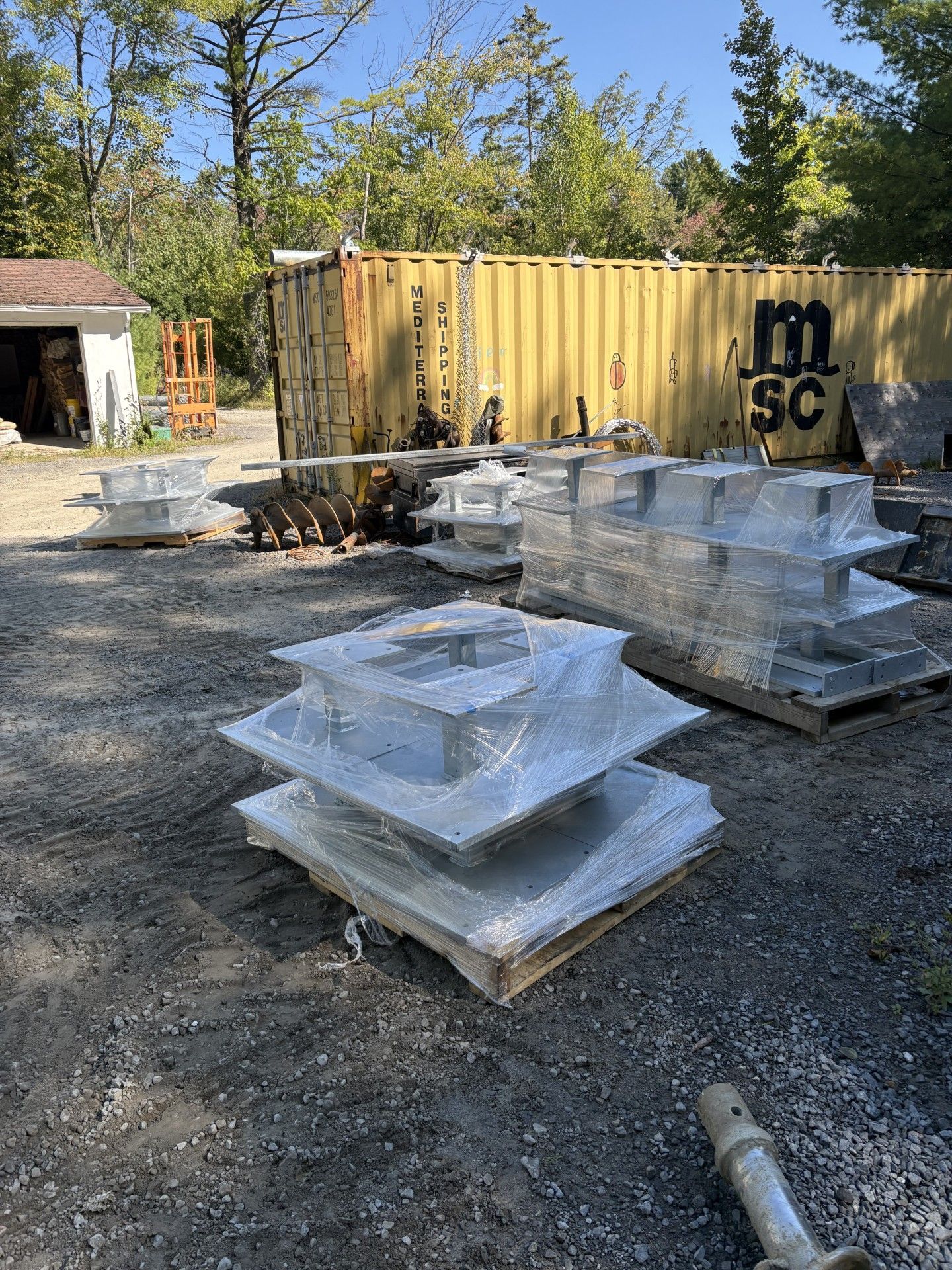 Pallets of gray stone blocks wrapped in plastic, outdoors. A yellow shipping container is in the background.