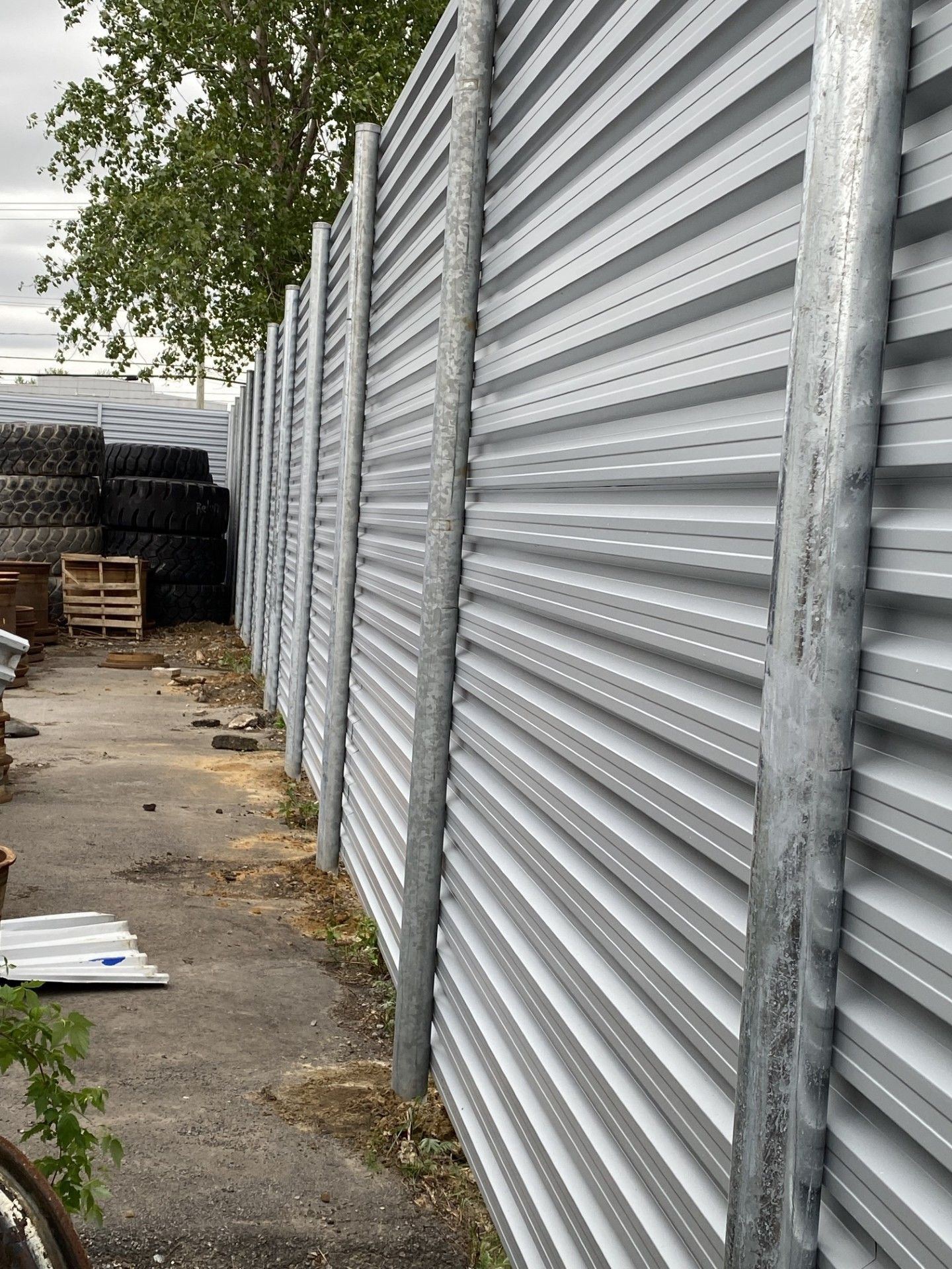Galvanized metal fence with vertical posts, running alongside a gravel area.