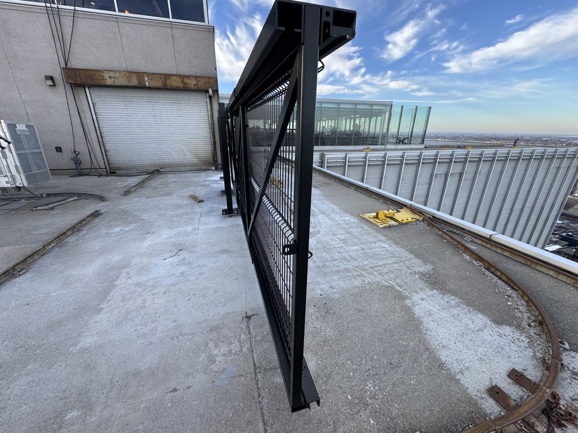 Black metal fence on a high building rooftop, sunny day with city view.