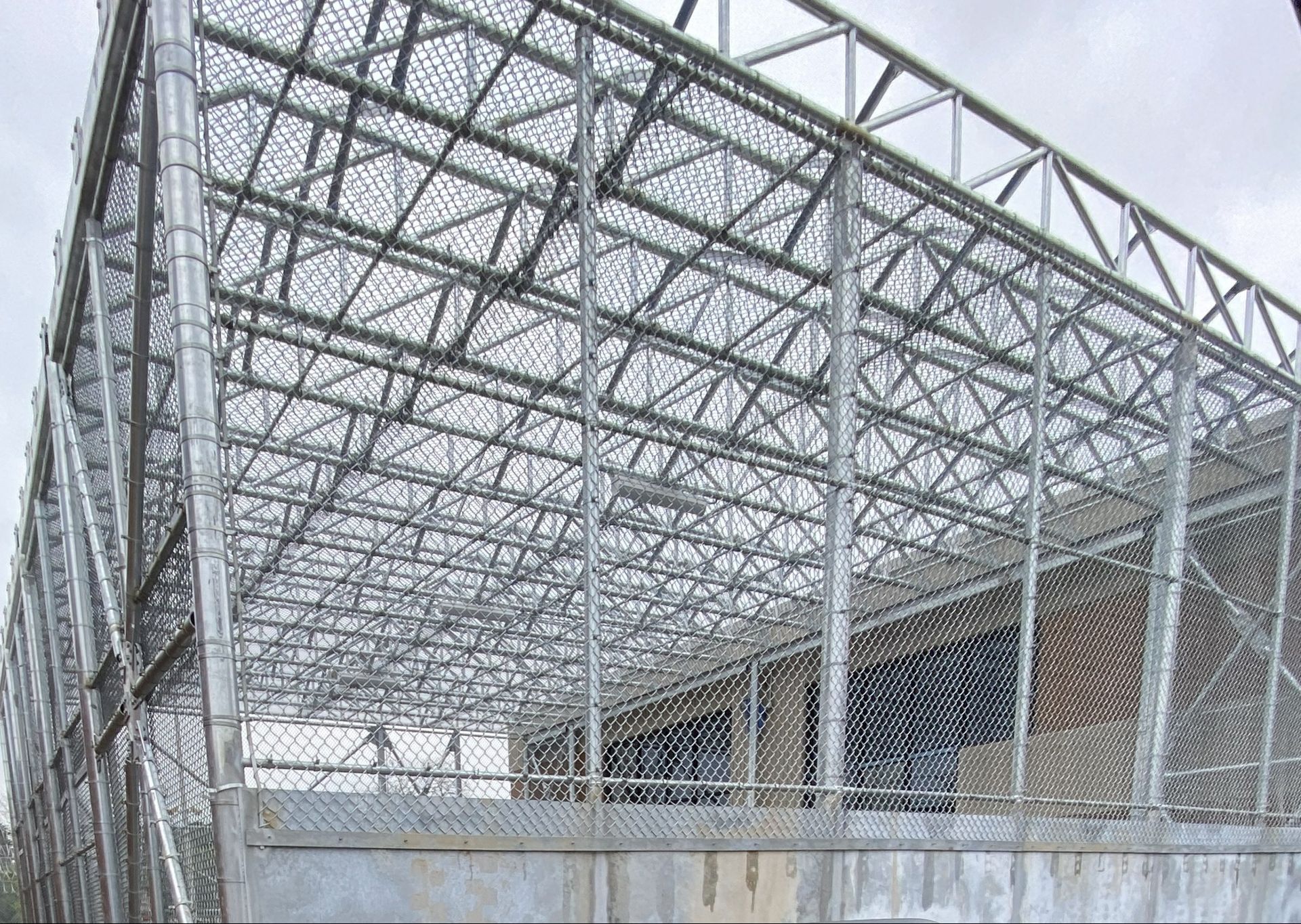 Metal fence structure covering a building; grey and silver, outdoor setting.