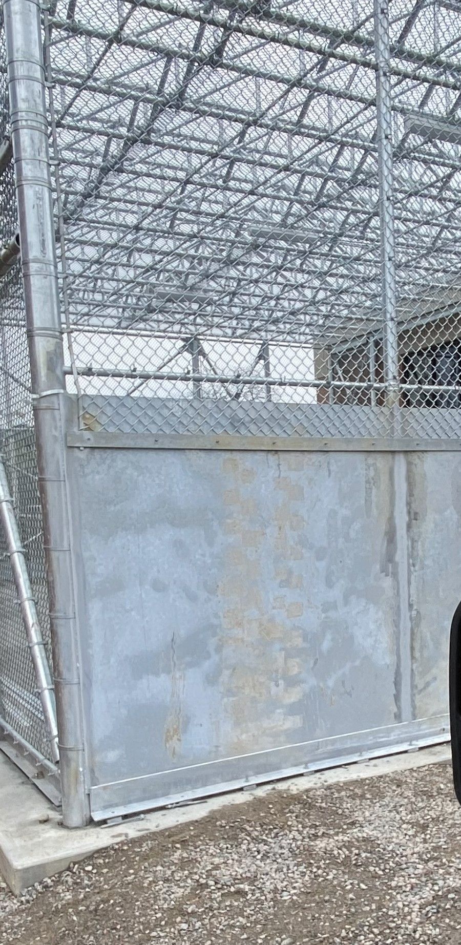Metal cage and gate with chain link fence. Grey metal door. Concrete base and gravel.