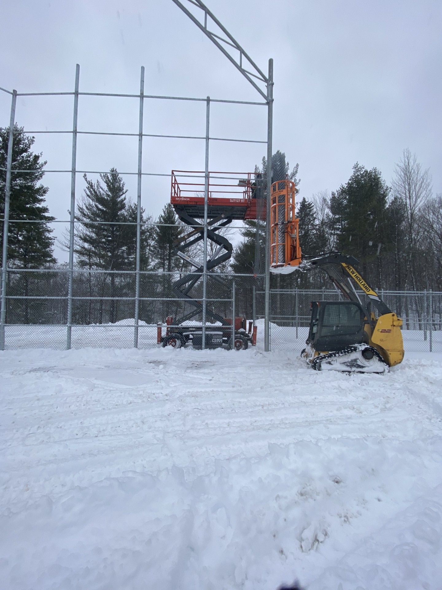 Construction site: lift with worker, metal framework, excavator, and snow.