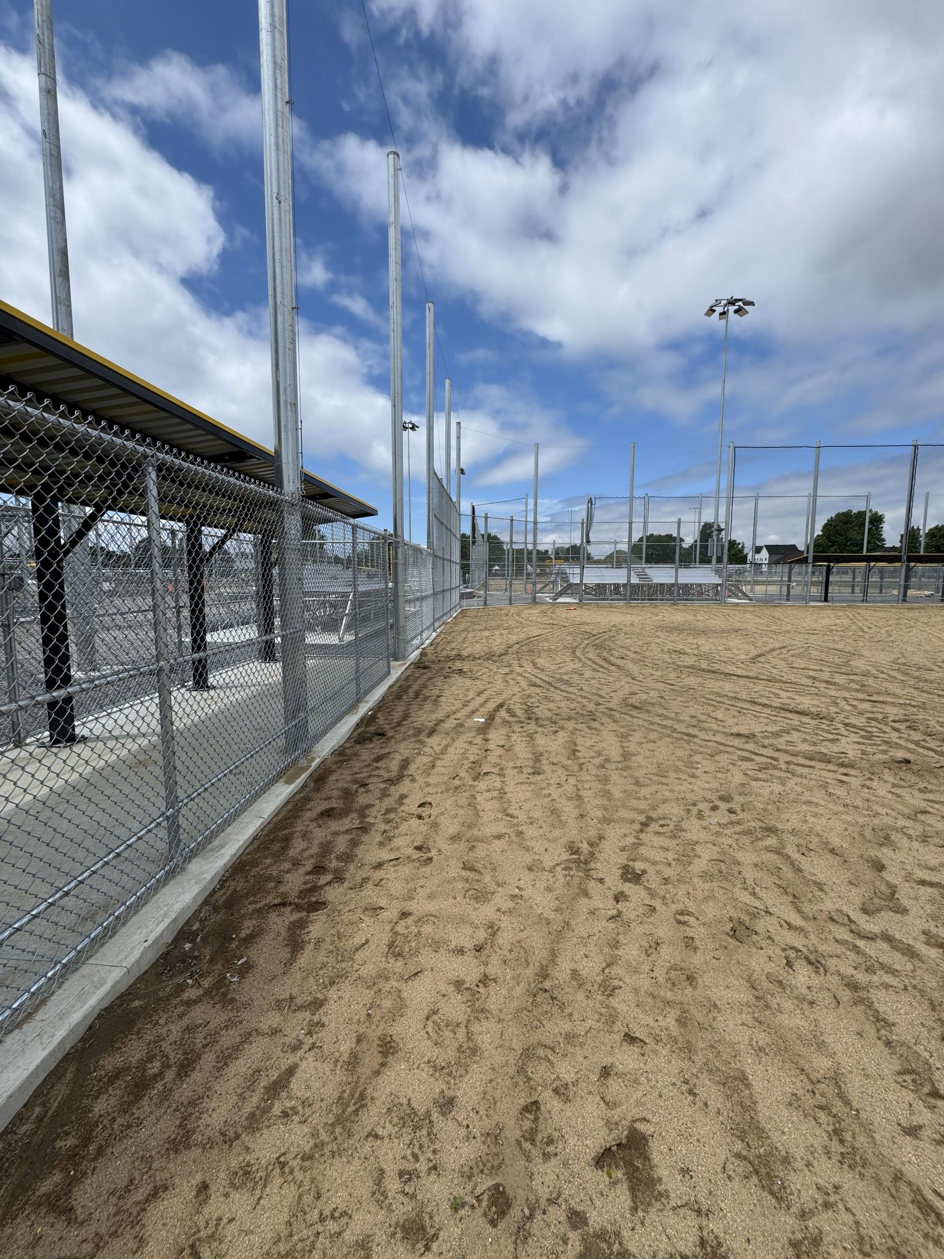 Sandy ground area next to a chain-link fence, under a partly cloudy blue sky.
