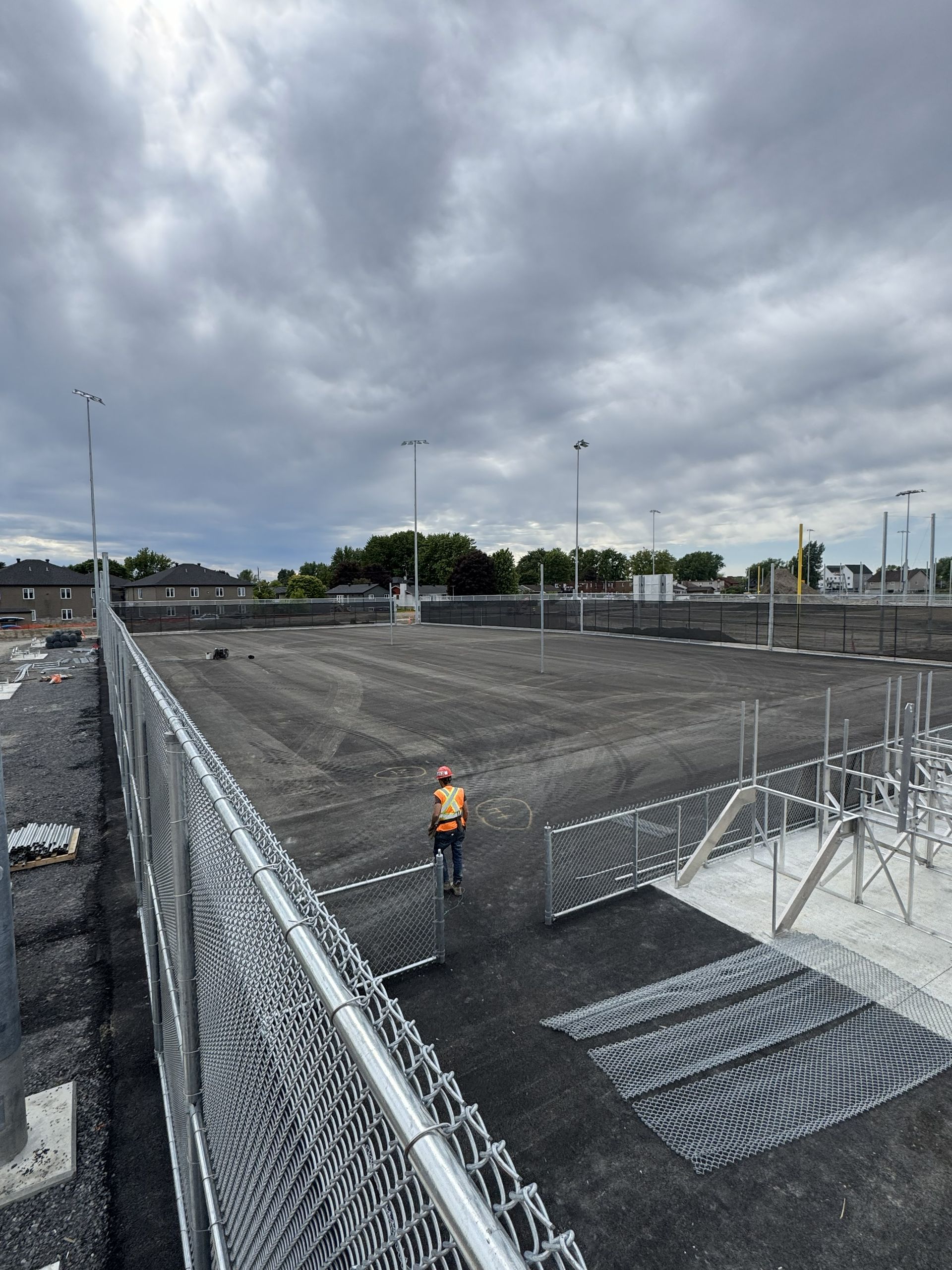Construction site with a fenced area, worker in vest, and cloudy sky.