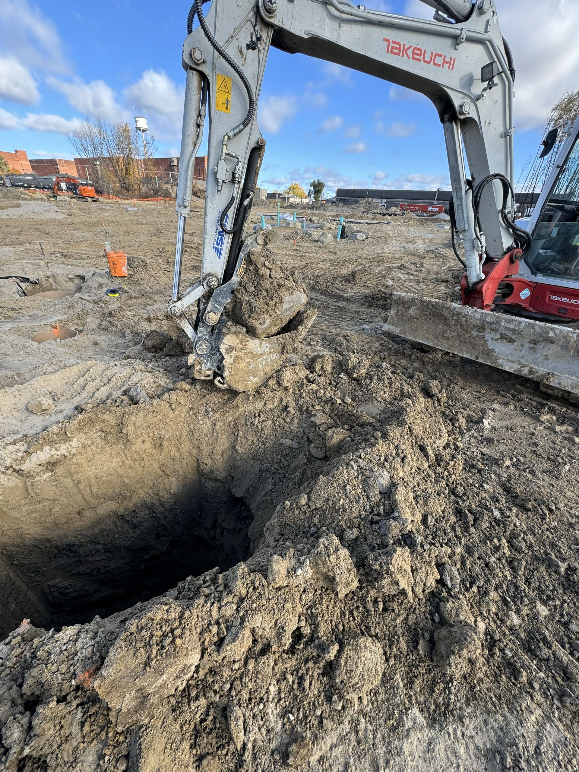 Excavator digging a hole in a construction site; overcast sky.