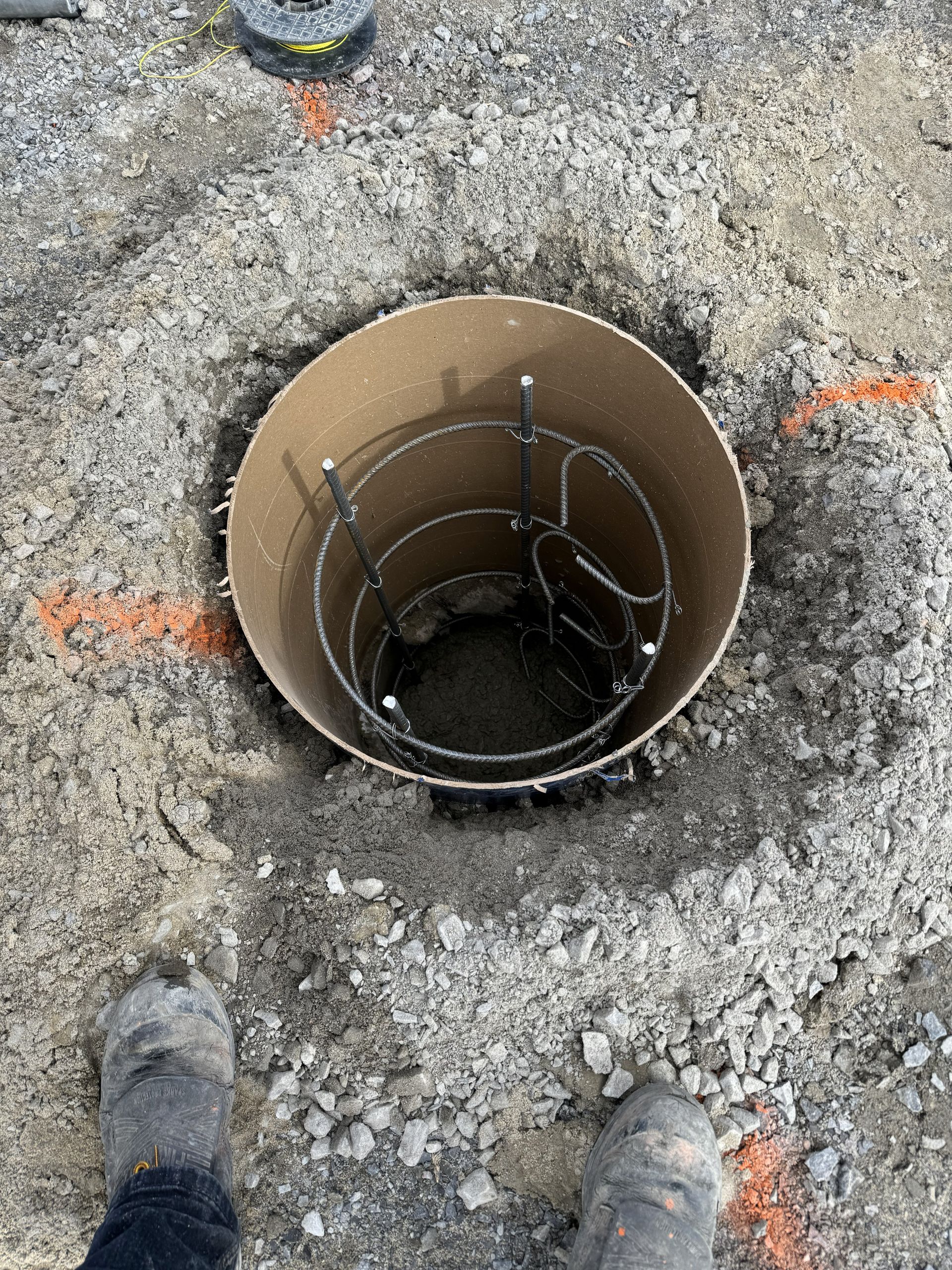 Footings and rebar inside a cardboard tube set in the ground. Orange markings around the hole.