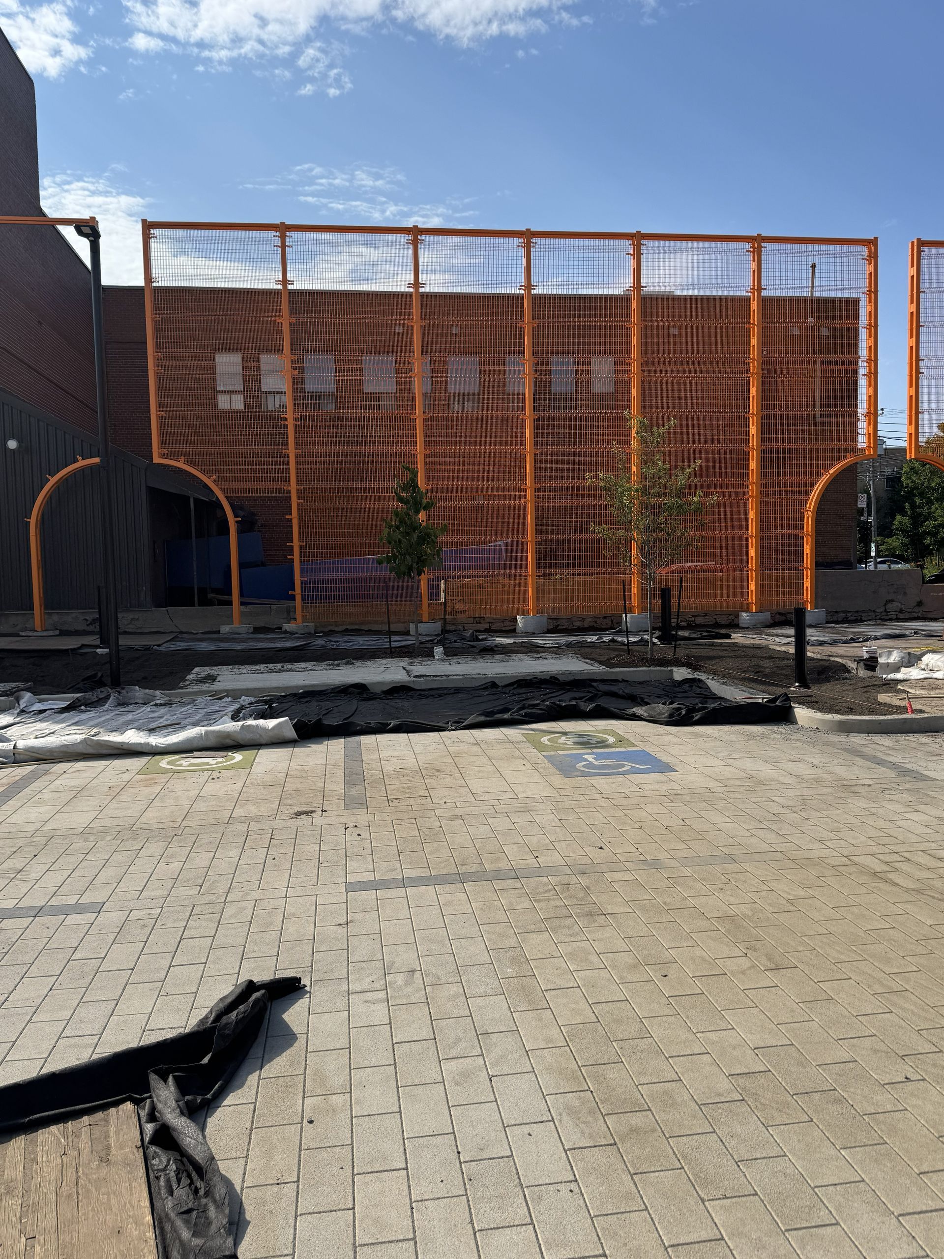 Orange metal framework in front of a brick building. Trees and debris on paved area.