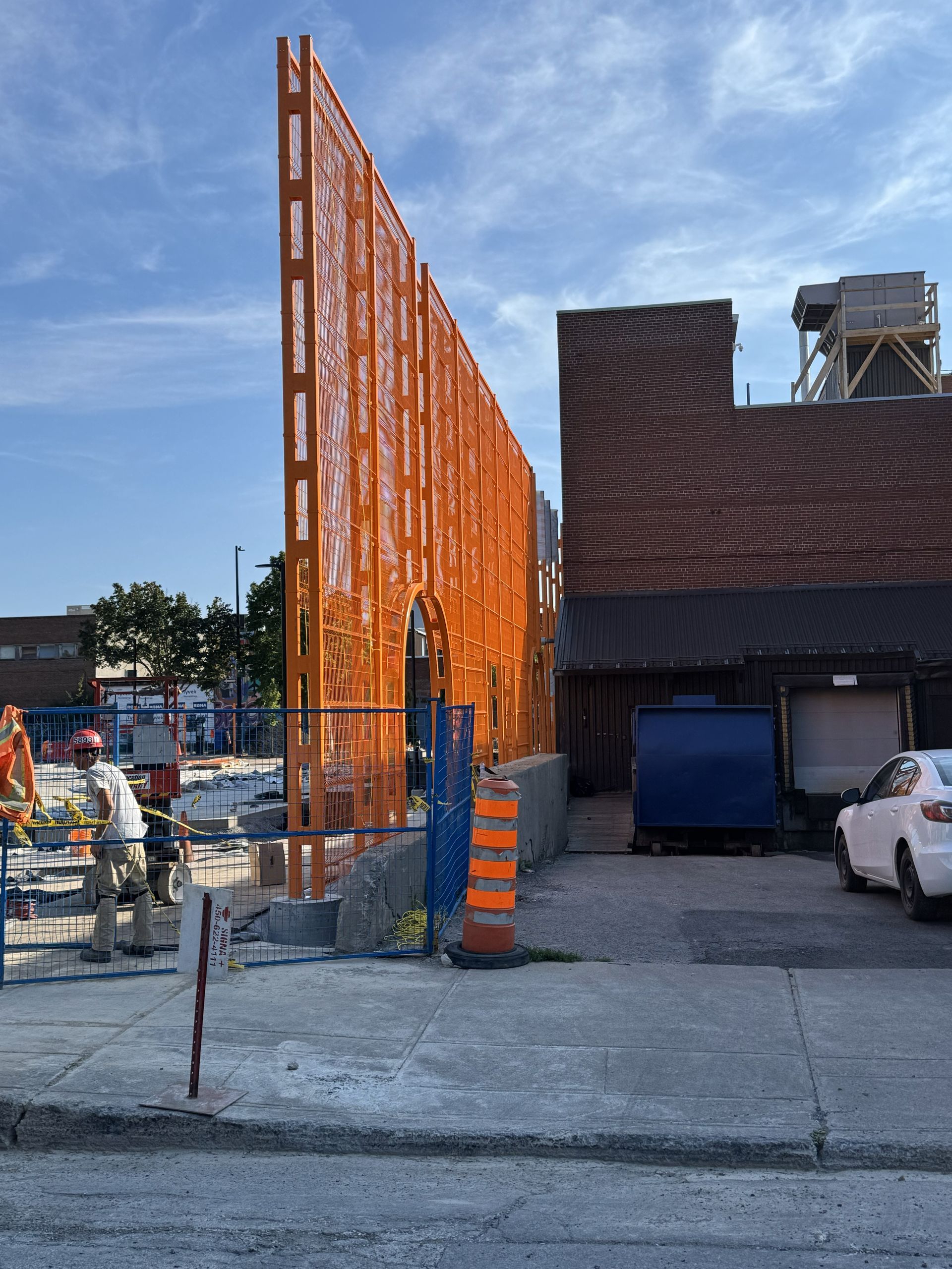 Orange perforated metal screen next to a brick building and a construction site.