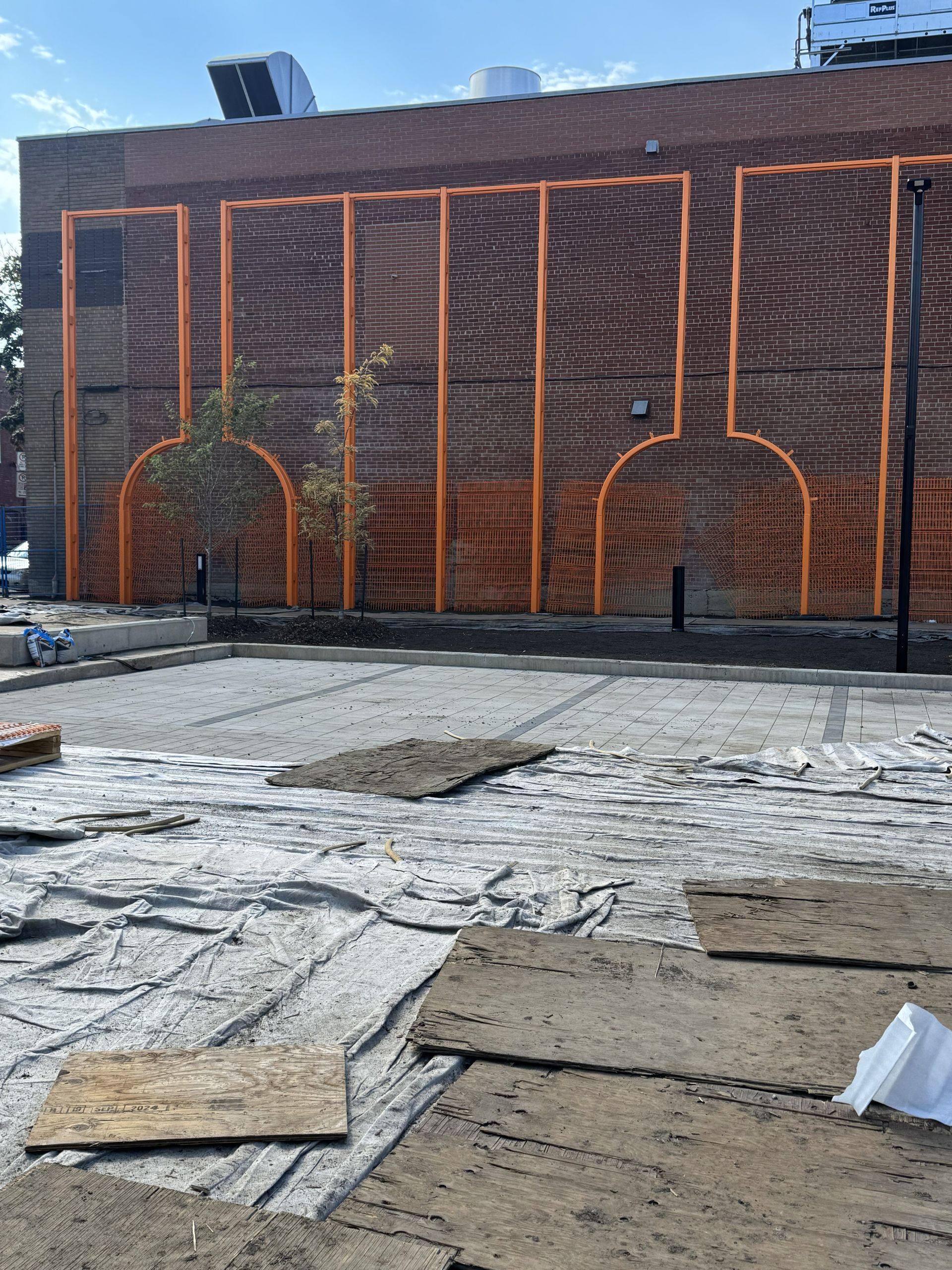 A brick building with orange metalwork design, a partially finished concrete area in front with building materials.