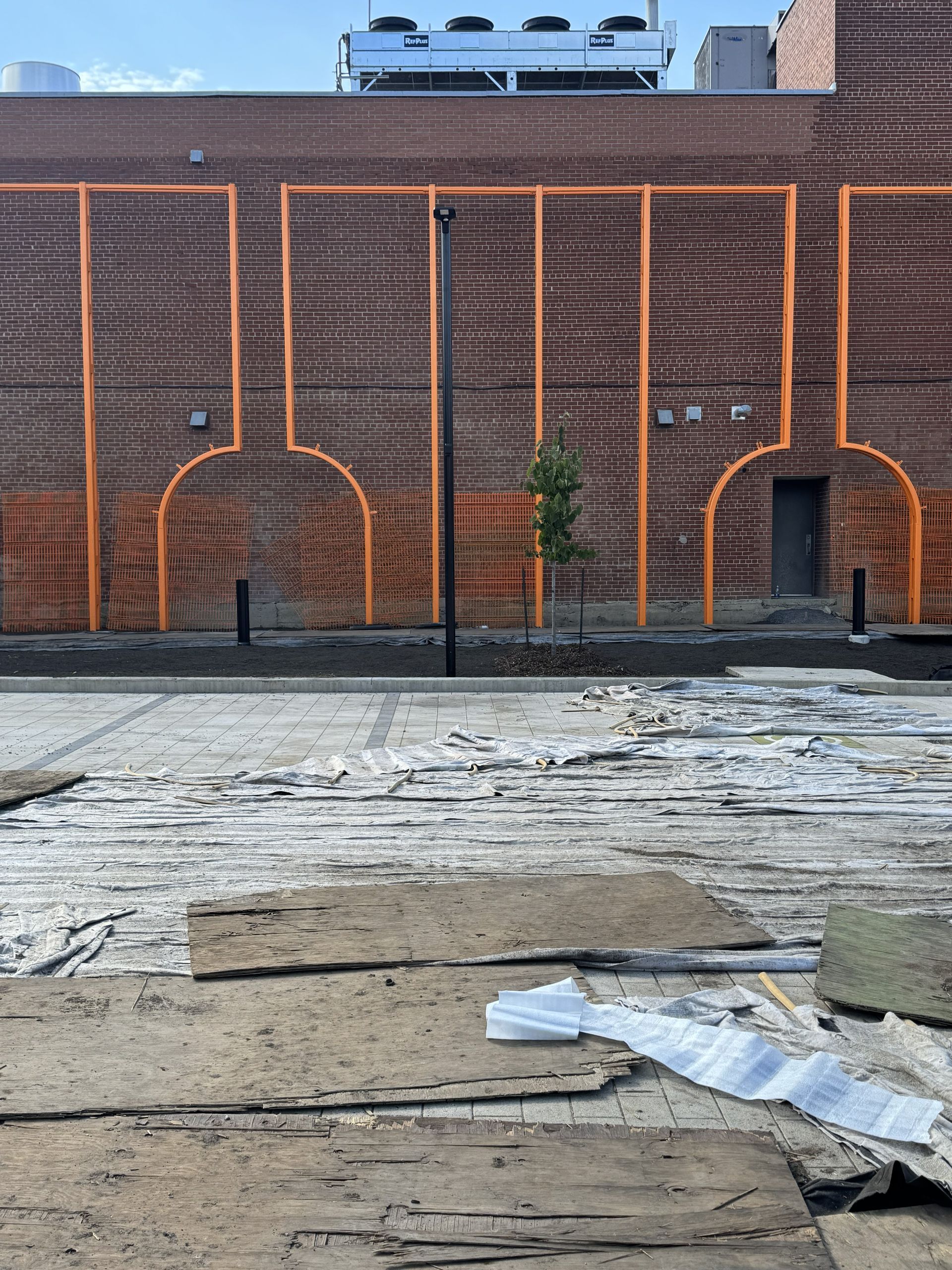 Brick wall with orange painted outlines, partially demolished ground, a lone tree, and a light pole.