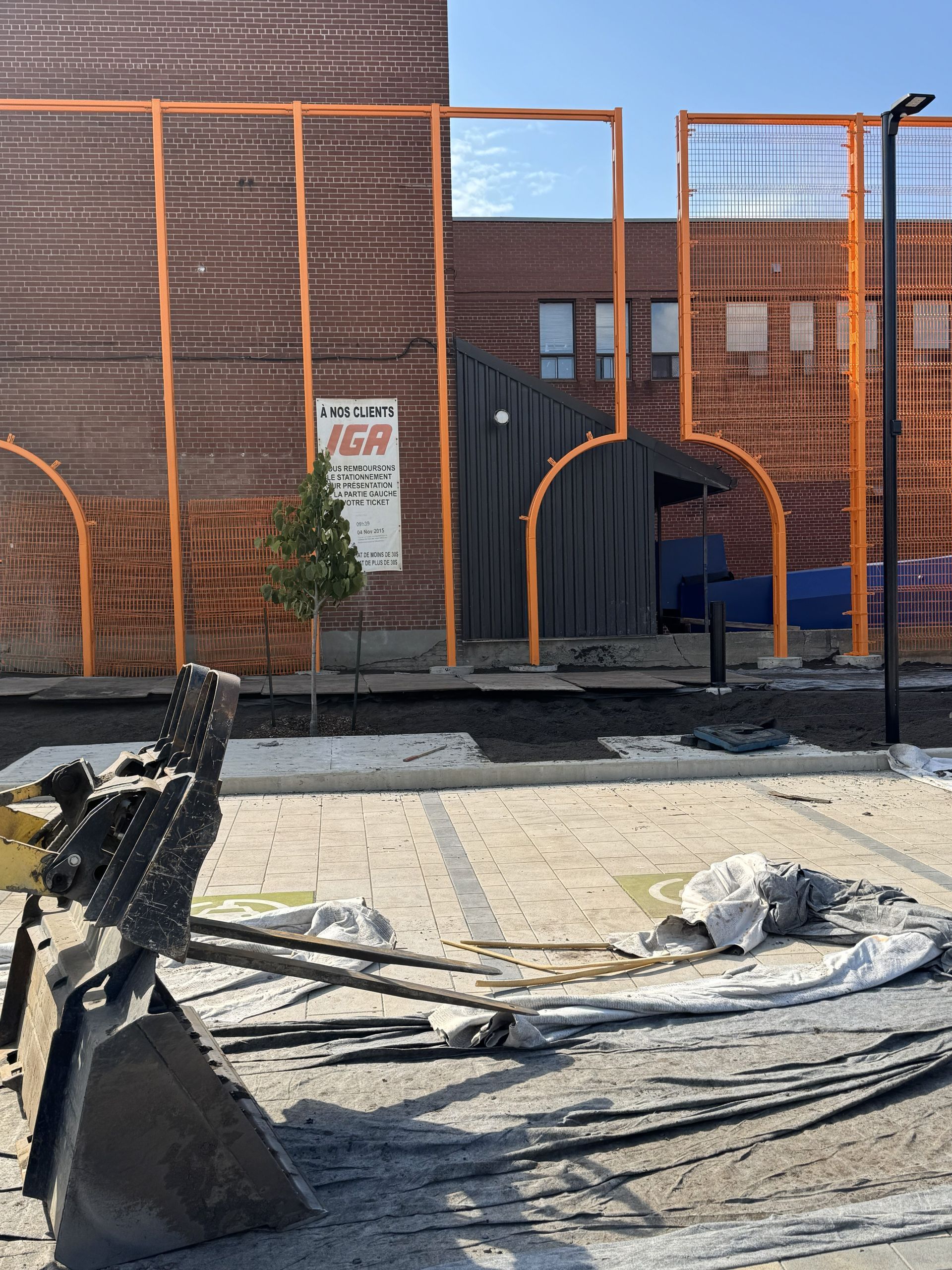 Construction site with orange fencing, brick building, and a backhoe in the foreground.
