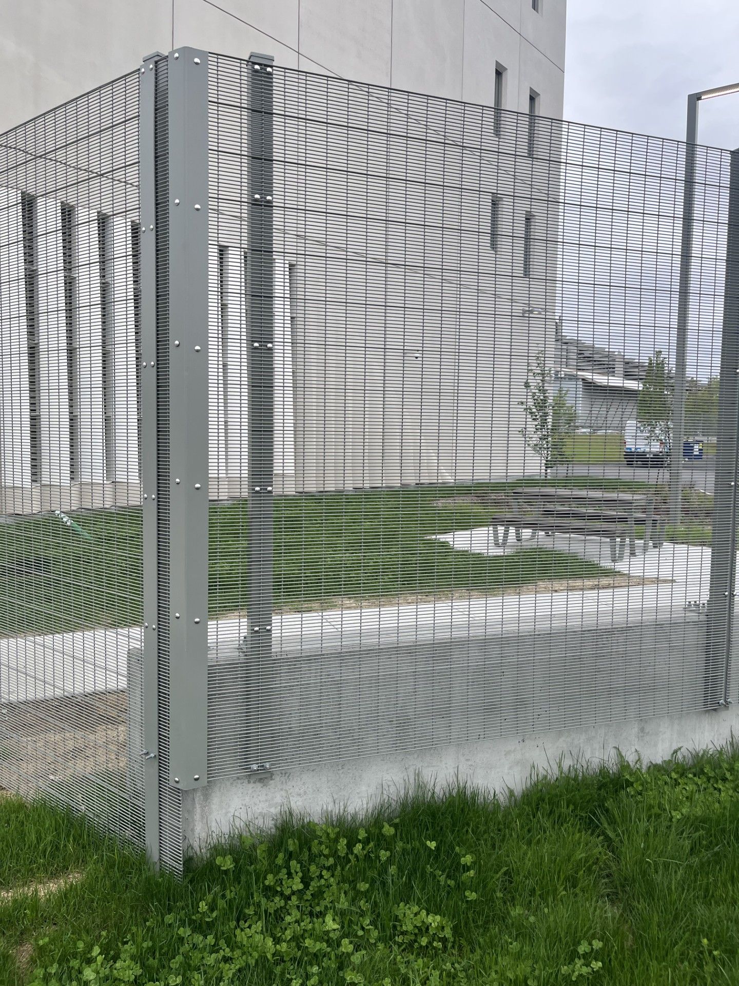 Metal security fence with wavy pattern on concrete and grass.