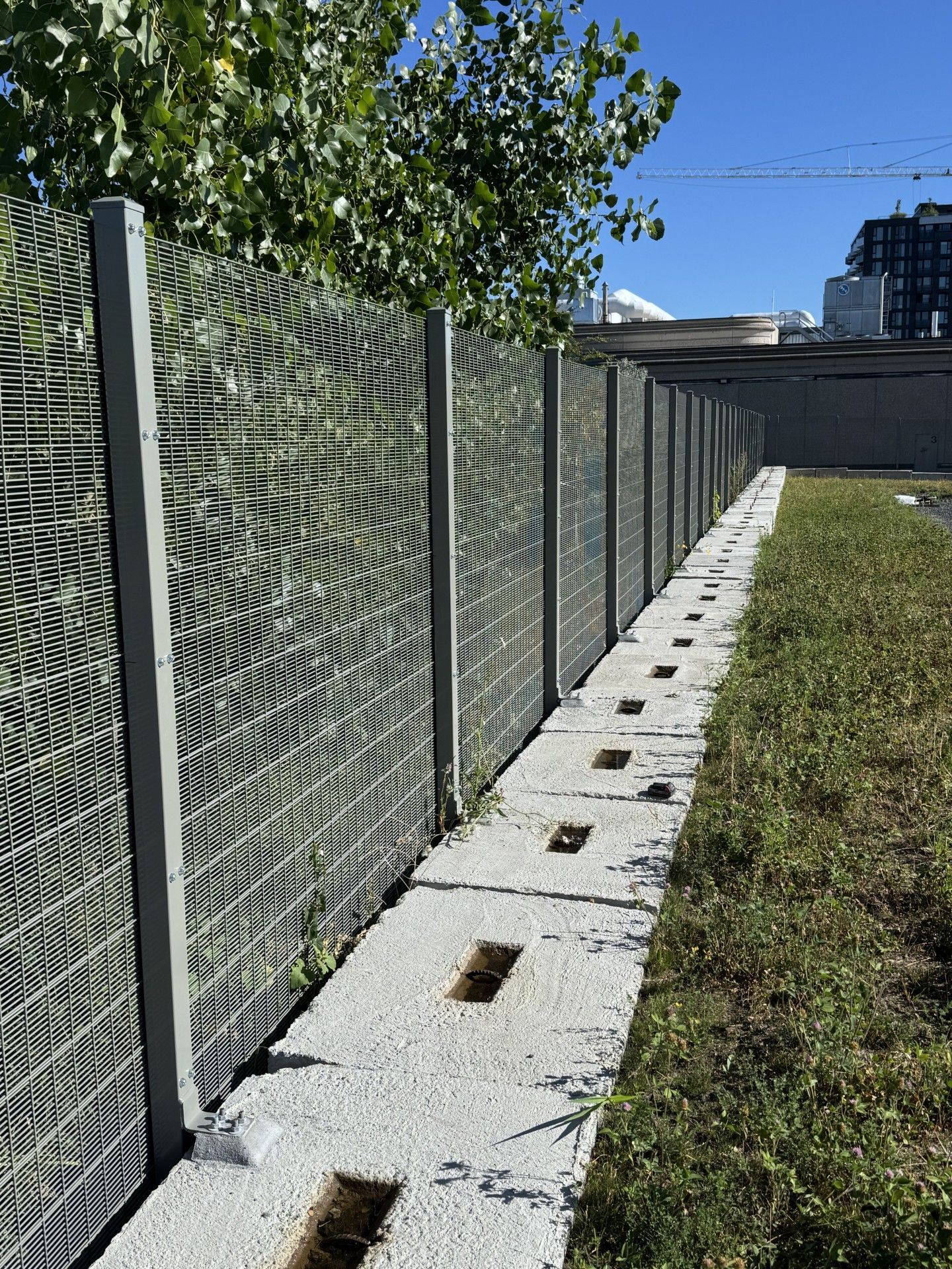 Gray metal fence with decorative panels, concrete base, and grass alongside.