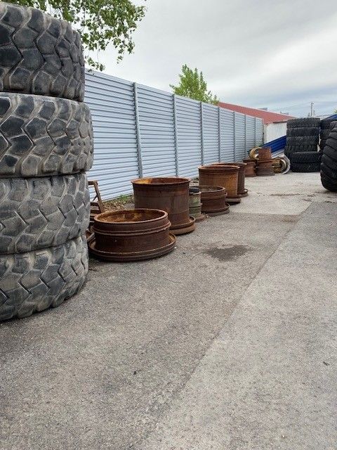 Tires stacked, rusted rims, and a fence on a paved surface, likely an industrial yard.