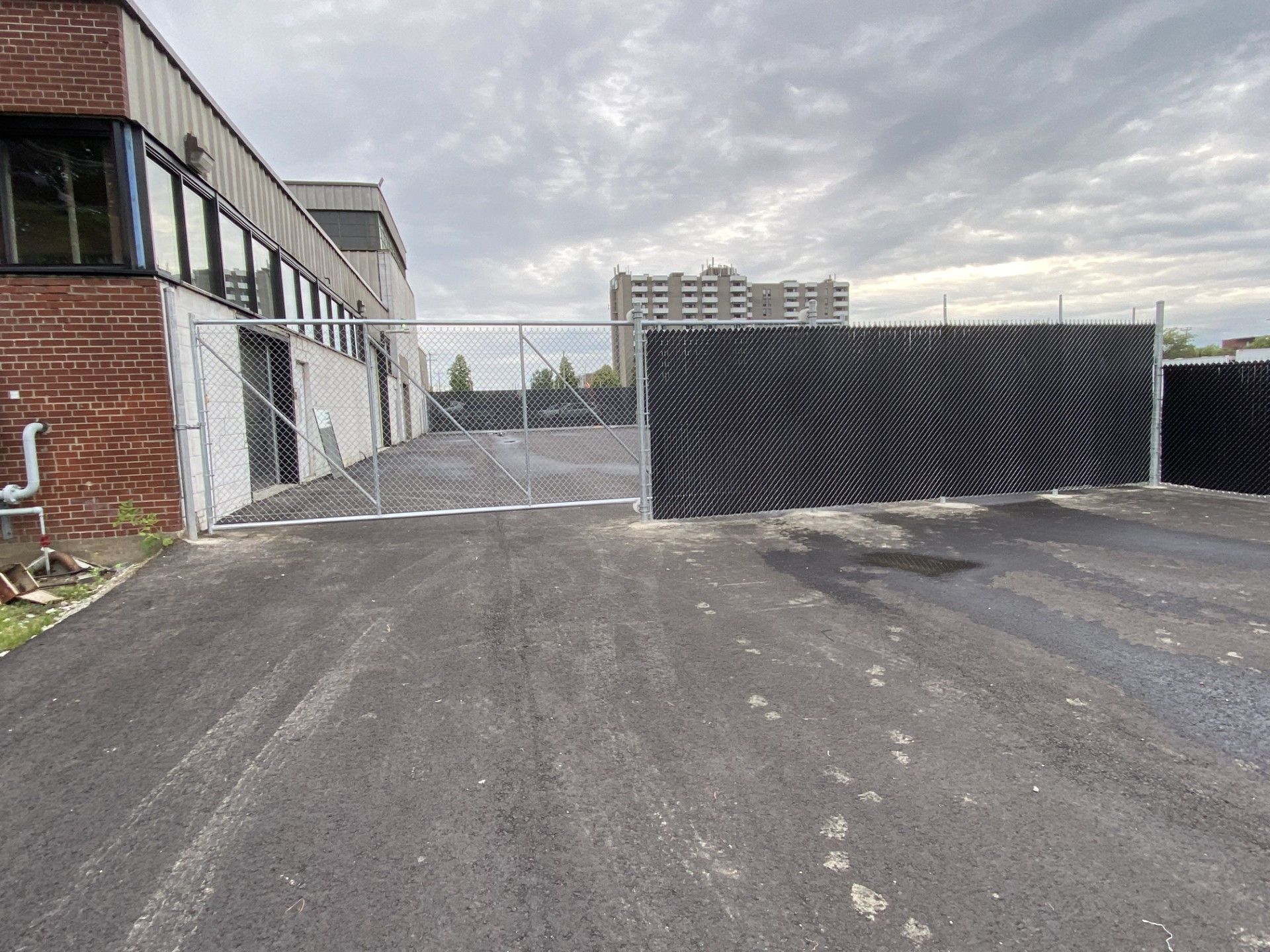 A paved area with a chain-link fence, a gate, and a building on a cloudy day.