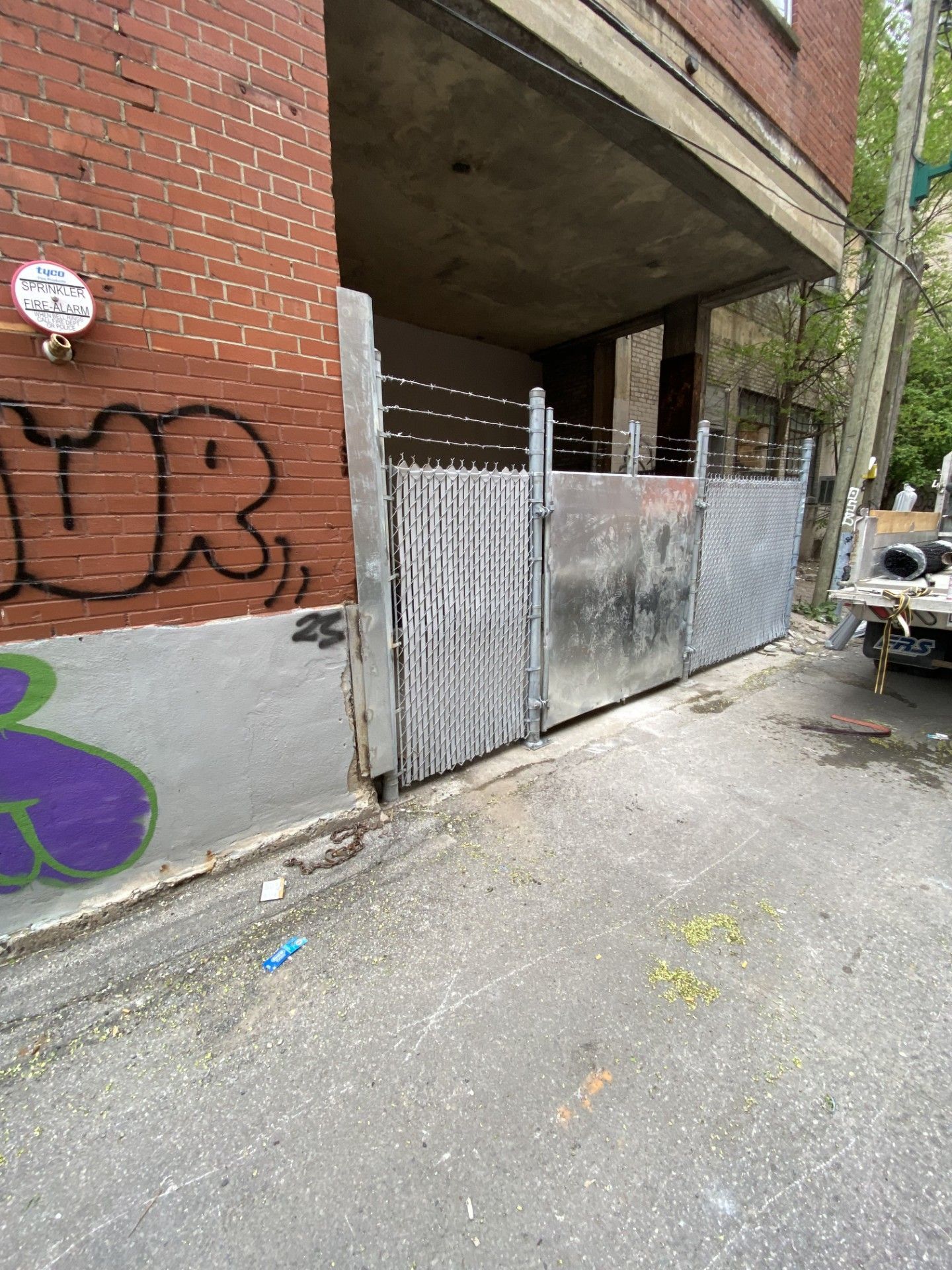 Metal gates blocking a passageway between brick buildings, graffiti on the walls.