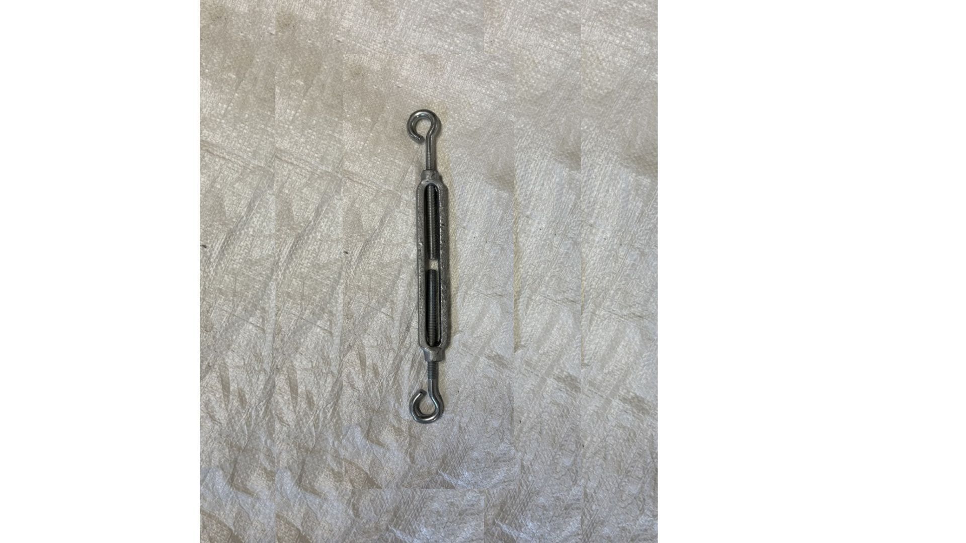 Le tendeur, un dispositif de fixation métallique utilisé pour ajuster la tension des cordes ou des câbles, repose sur une surface texturée.