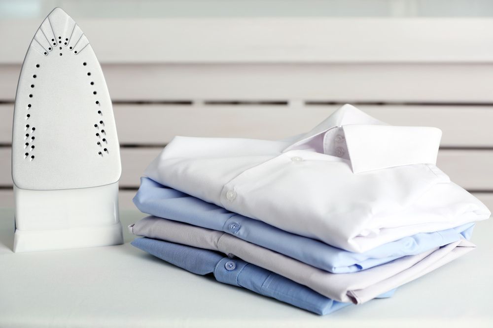 A Stack of Shirts Next to An Iron on A Table — Ezy Laundrette Diamond Beach in Diamond Beach, NSW