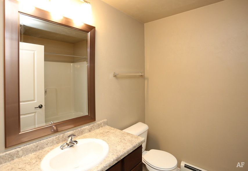 Small bathroom with a vanity sink, large mirror, toilet, and beige walls.