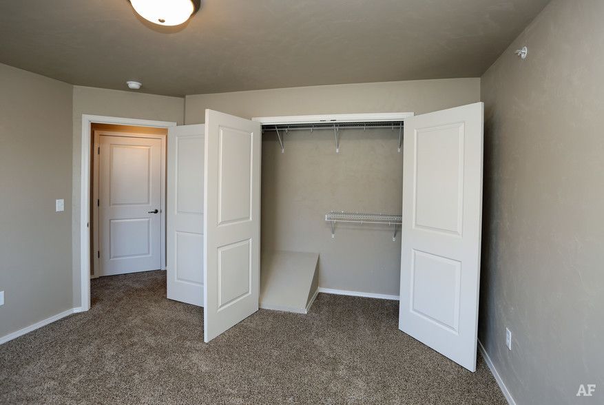 Empty beige bedroom with open closet doors and carpeted floor