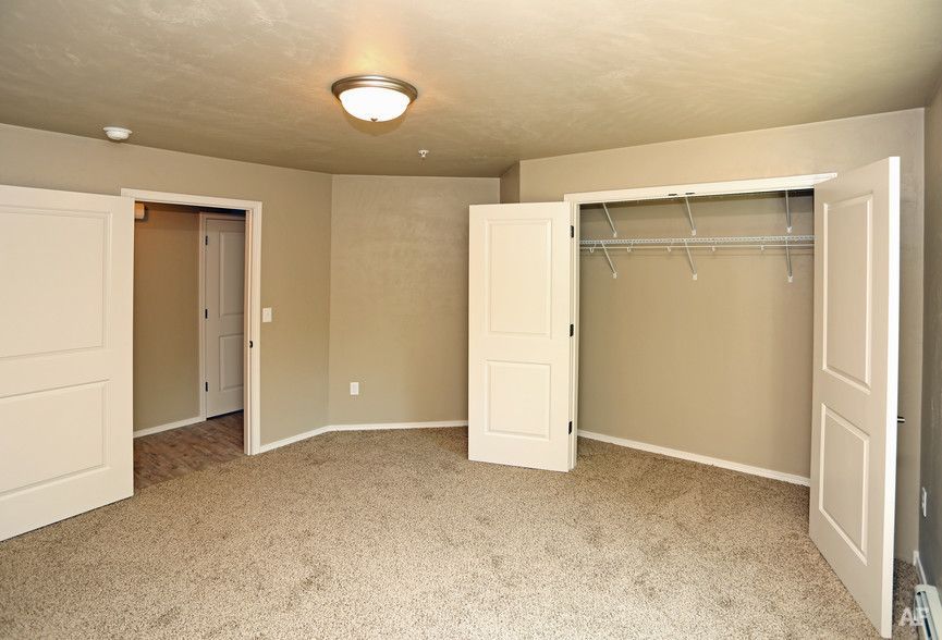 Empty beige bedroom with open closet doors and carpeted floor