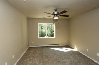 Empty beige carpeted living room with a ceiling fan and a window letting in sunlight