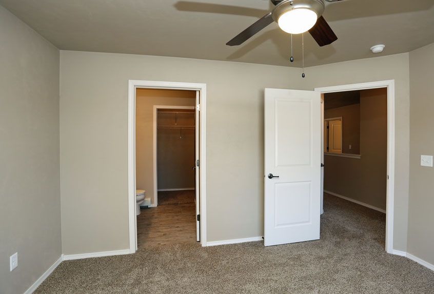 Empty carpeted bedroom with ceiling fan and two open doorways leading to closets or adjoining rooms