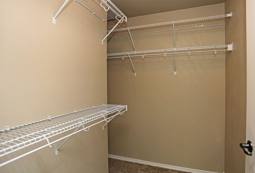 Empty beige walk-in closet with white wire shelving on three walls