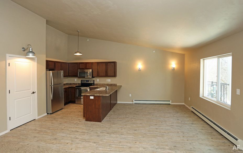Empty beige living room with kitchen, island, and large window lighted by wall sconces