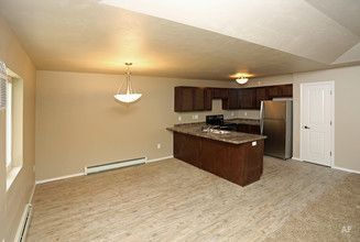 Empty kitchen and dining area with beige carpet, brown cabinets, and stainless steel refrigerator.