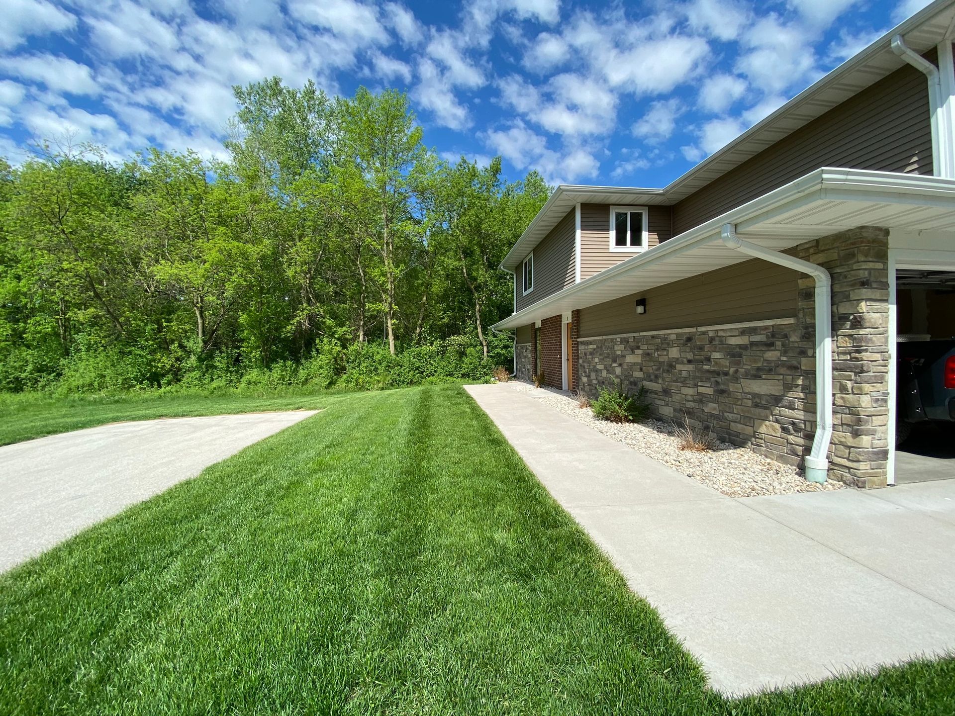 Suburban house with driveway, lawn, and trees under a blue sky