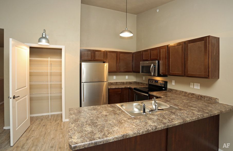 Empty kitchen with stainless appliances, dark wood cabinets, granite island, and open pantry door.