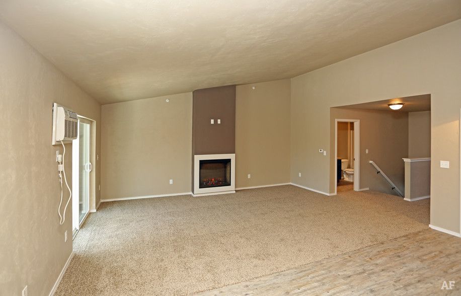 Spacious beige living room with carpet, fireplace, and doorway to hallway and stairs