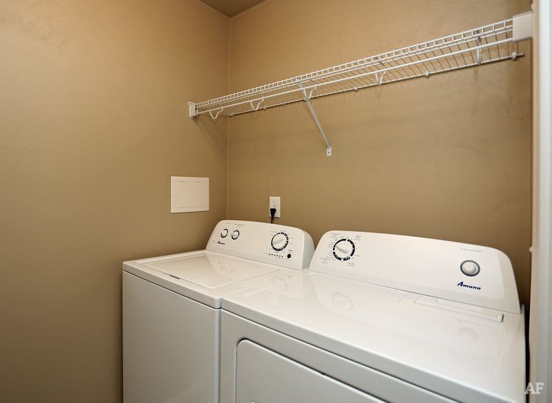 Laundry room with white washer and dryer under a wire shelf on beige walls