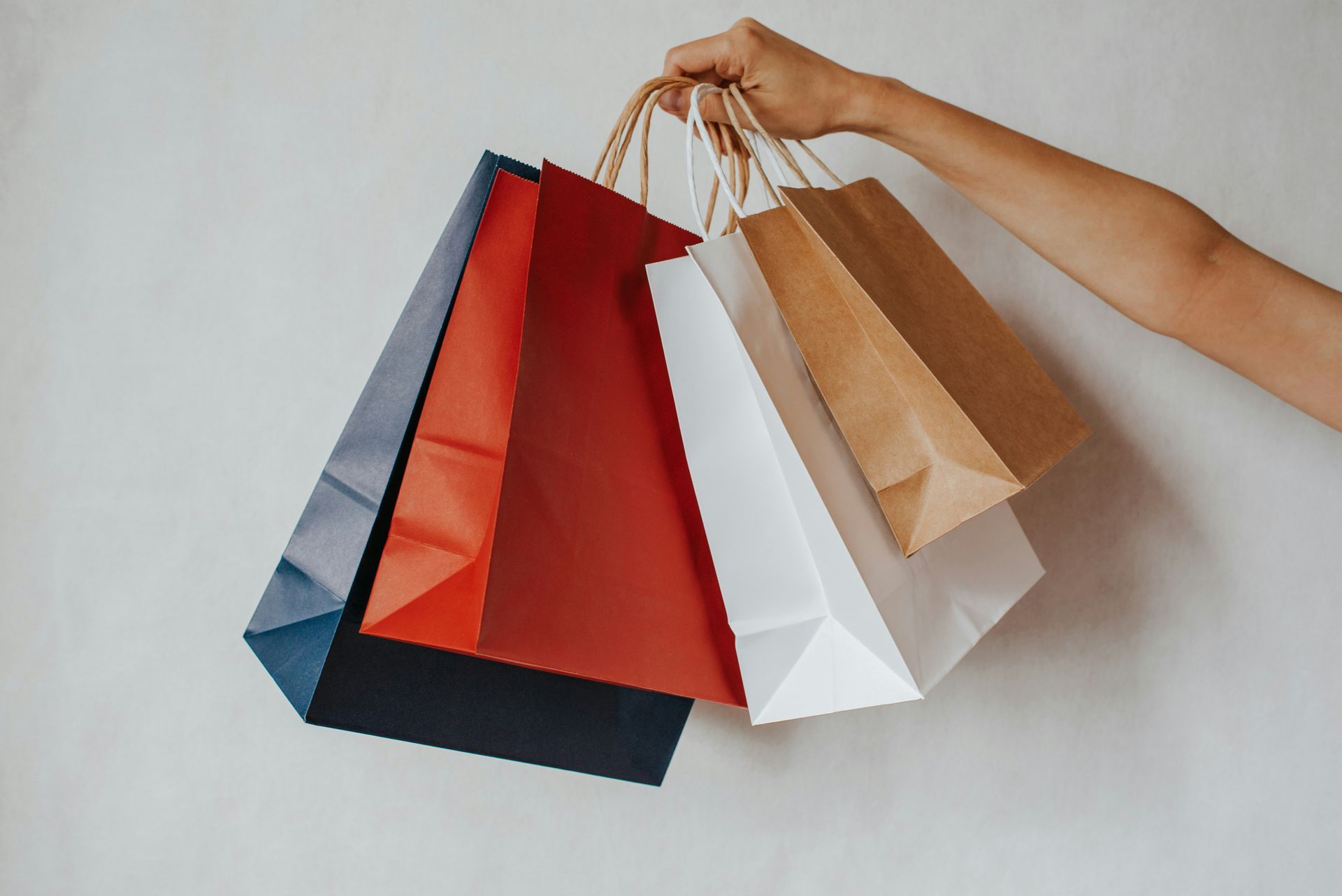 Hand holding several colorful shopping bags against a plain background