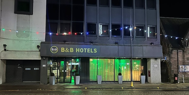 B&B Hotels building at night with string lights above the entrance, green interior glow.