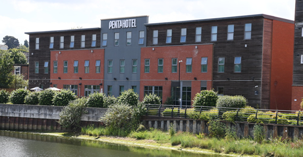 Penta Hotel exterior; multi-story building with brick and wood facade, blue sky, situated near water.